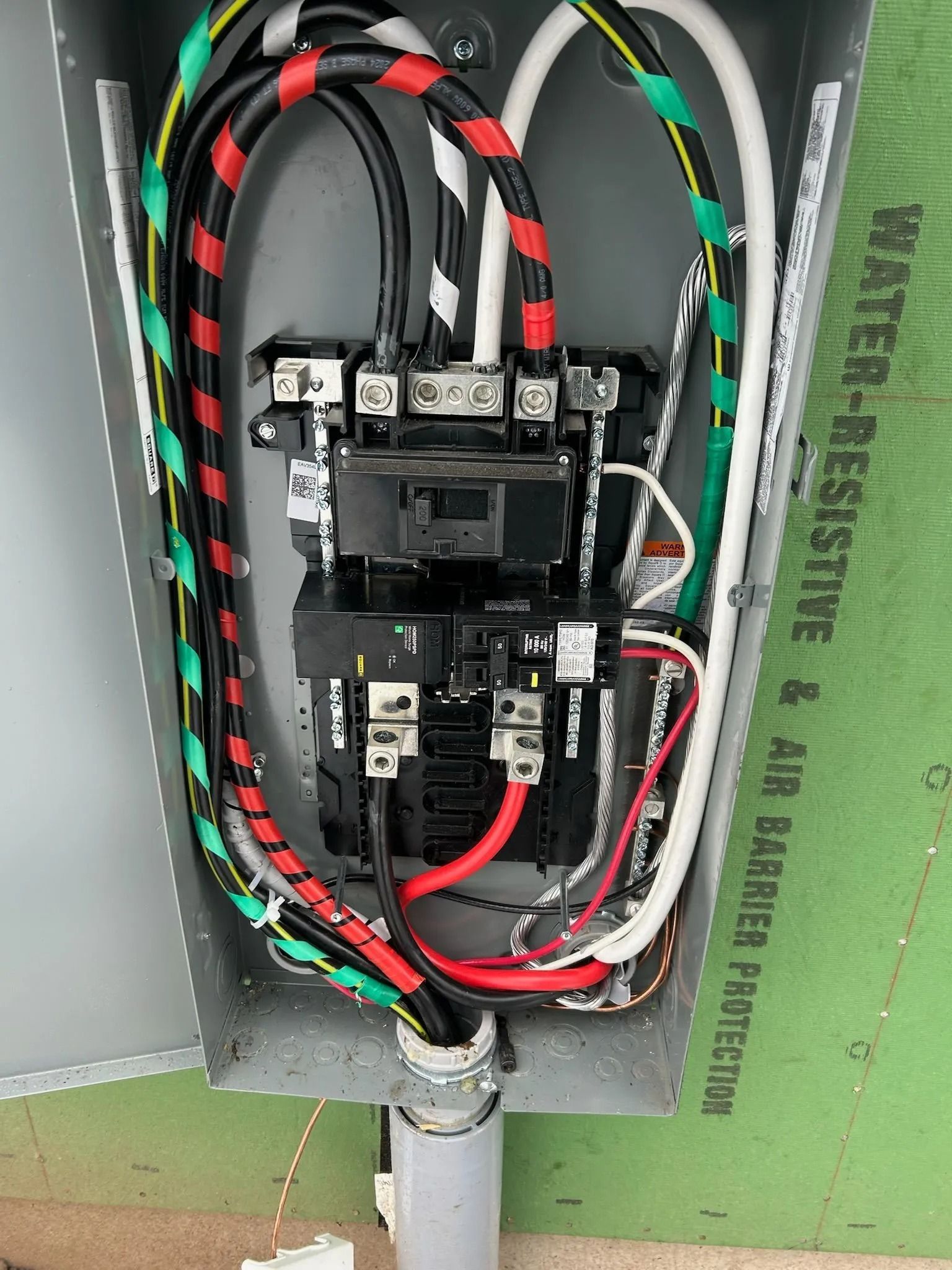 Electrical panel with colored wires and circuit breakers inside a metal box.