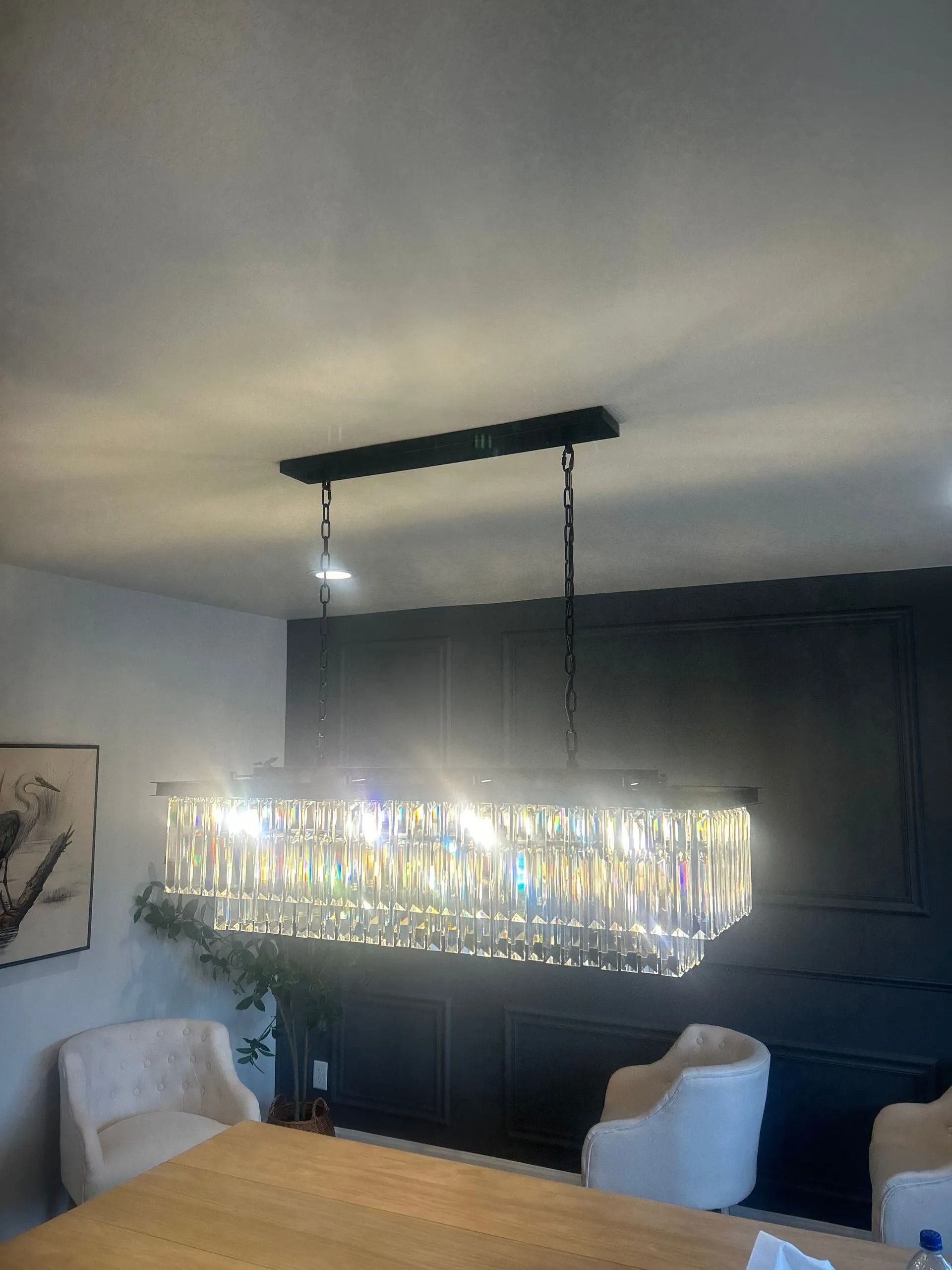 Rectangular crystal chandelier over a dining table, black ceiling fixture, two white armchairs.