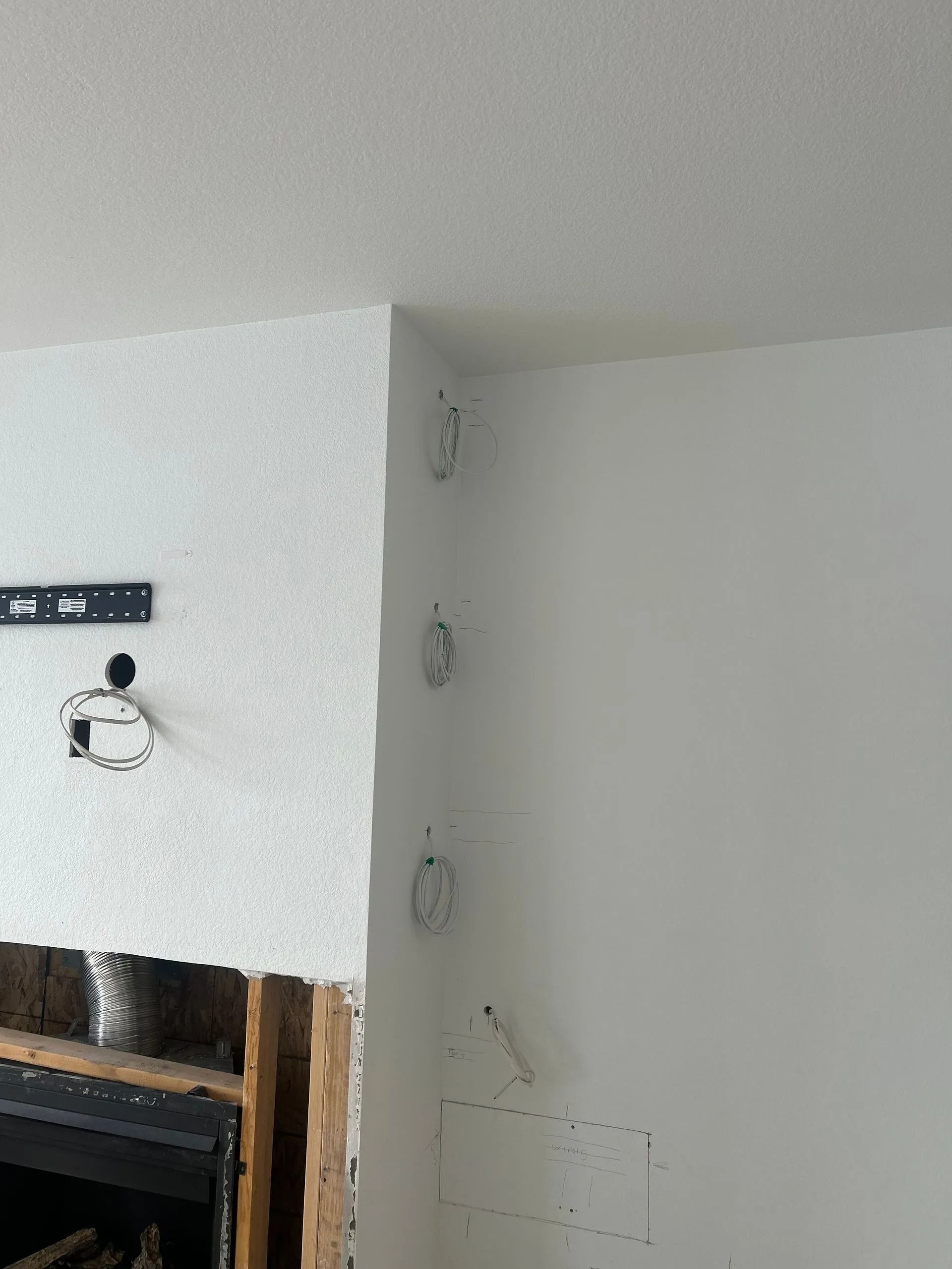 White walls with electrical wires extending from the ceiling and a partially constructed fireplace below.