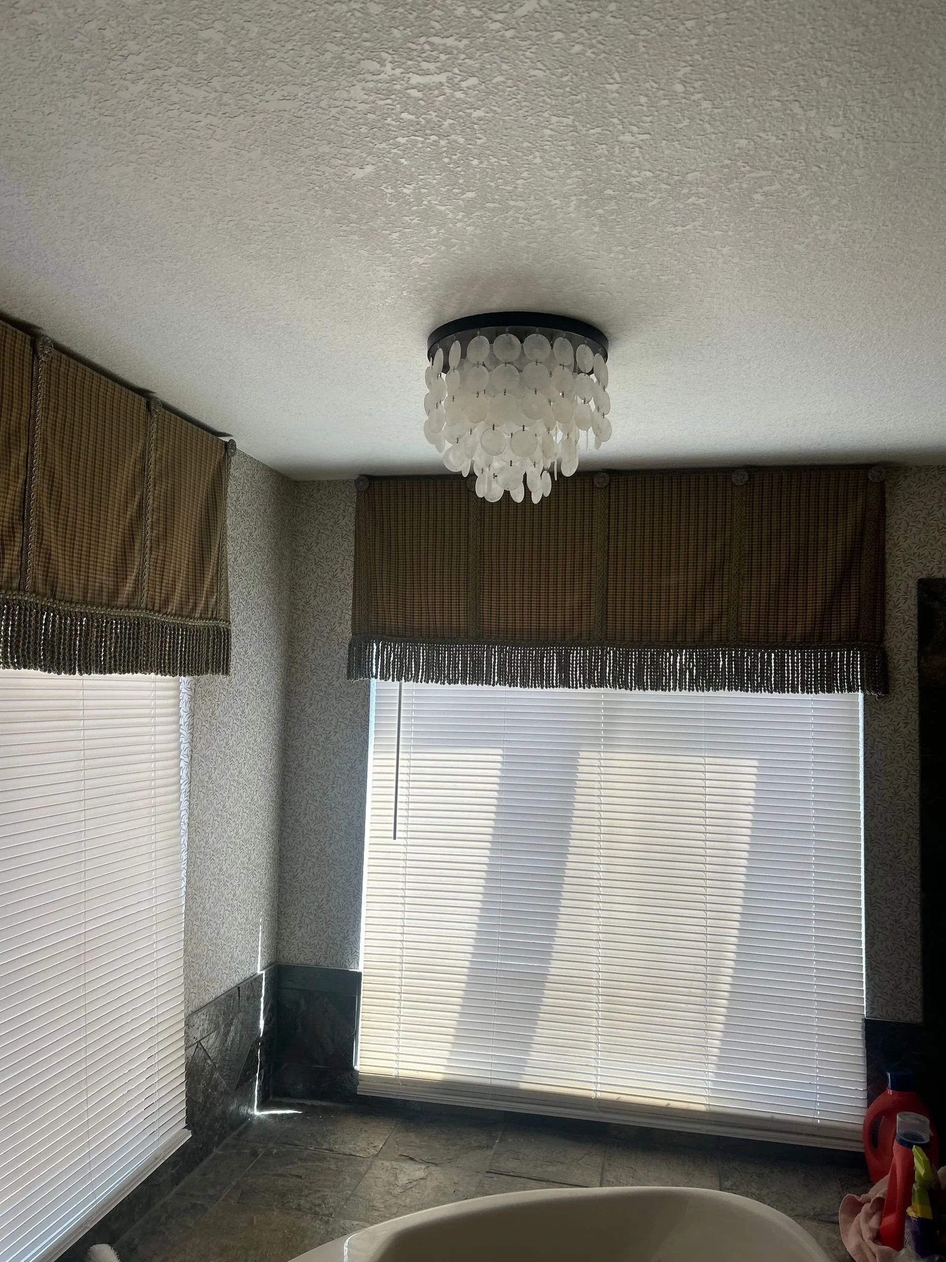 Bathroom with a shell-like chandelier, two windows with woven shades over blinds.