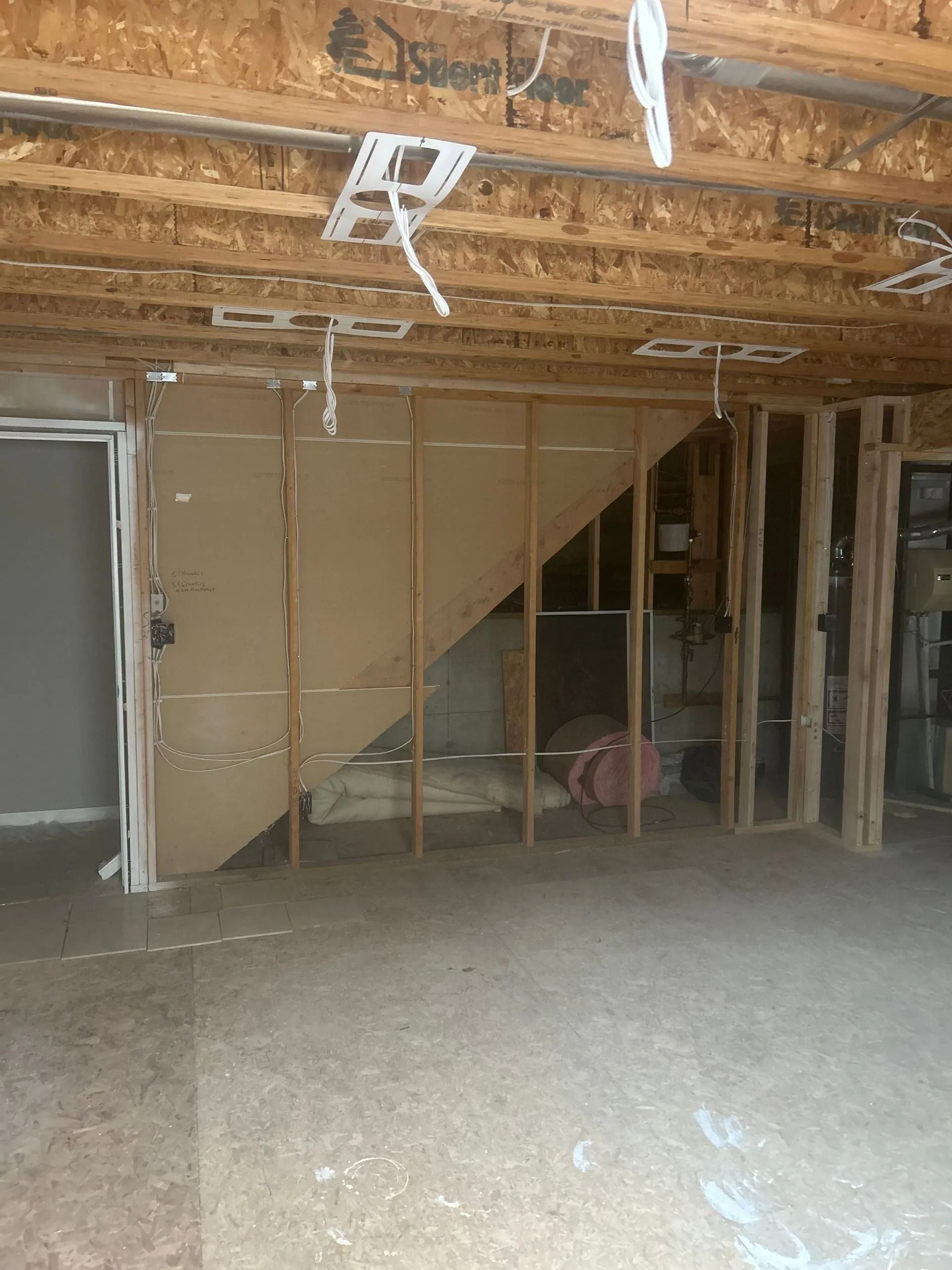 Interior under construction: partially framed walls, unfinished ceiling, visible stairwell.