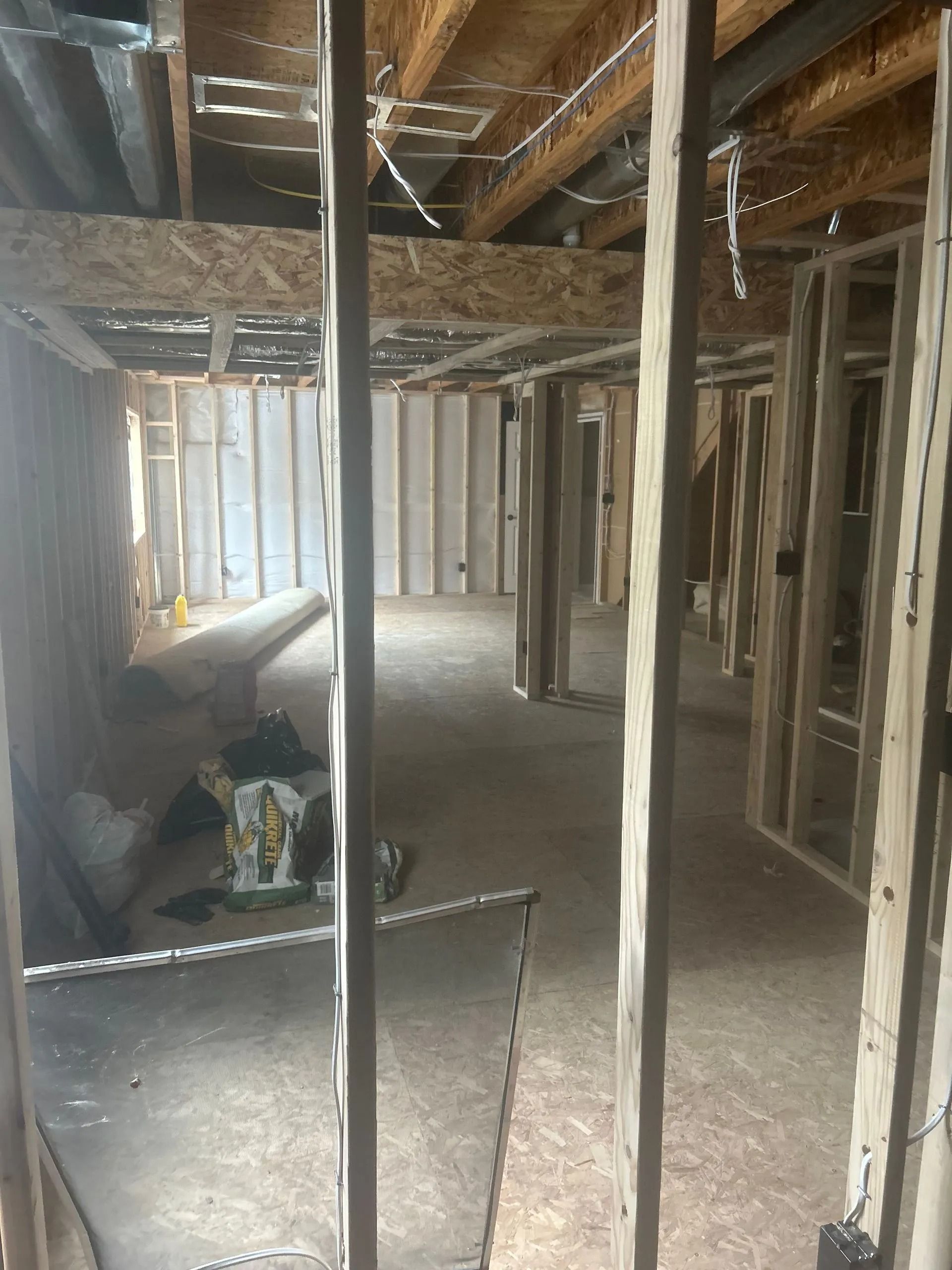 Interior framing of a building under construction, showing wooden studs, beams, and an open floor plan.