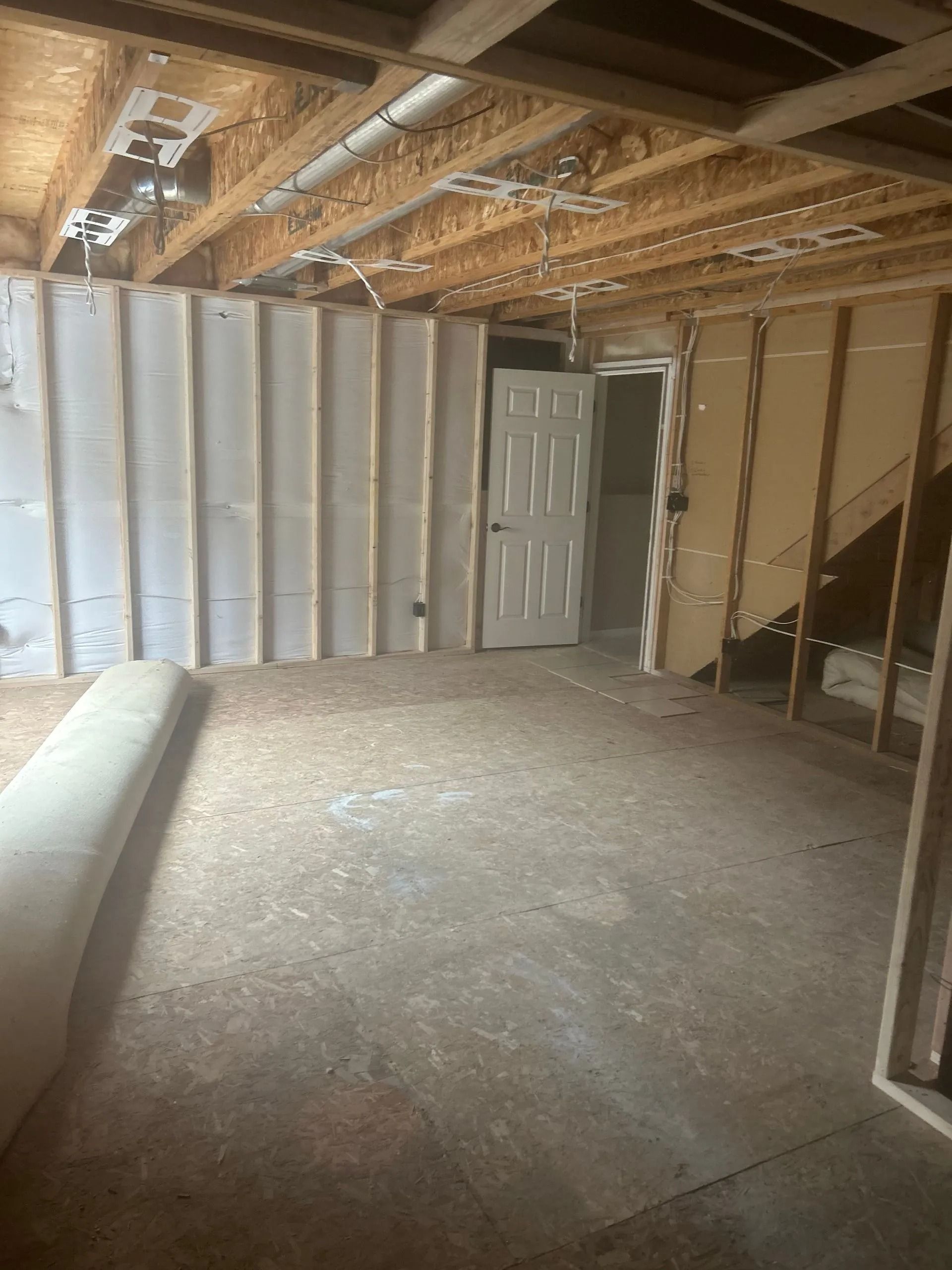 Interior view of a room under construction with exposed beams, drywall, a door, and a concrete floor.