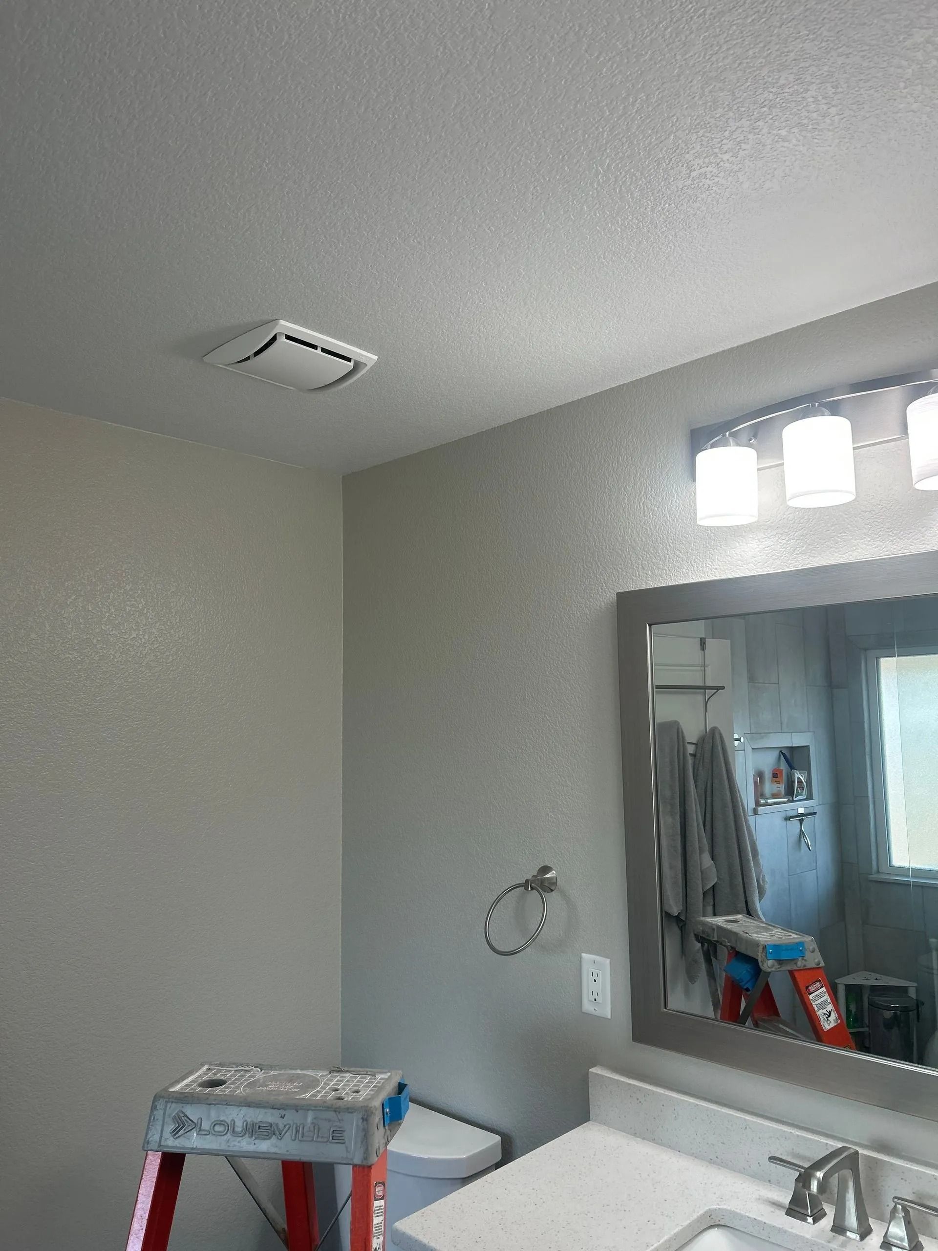 Bathroom with a vanity, mirror, toilet, and vent. A stepladder sits near the toilet.