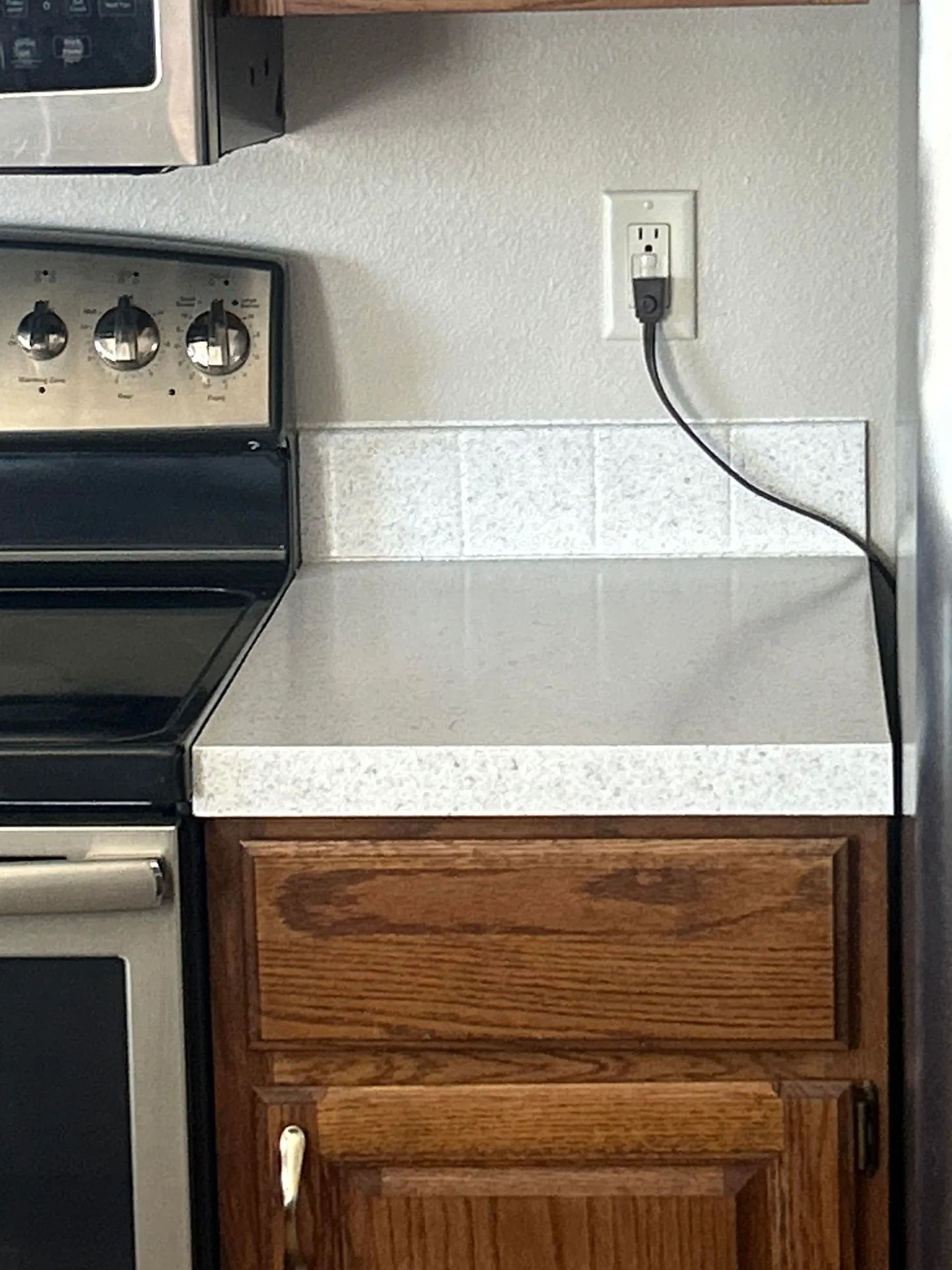 Kitchen counter and cabinets with an outlet and a plugged-in appliance cord.