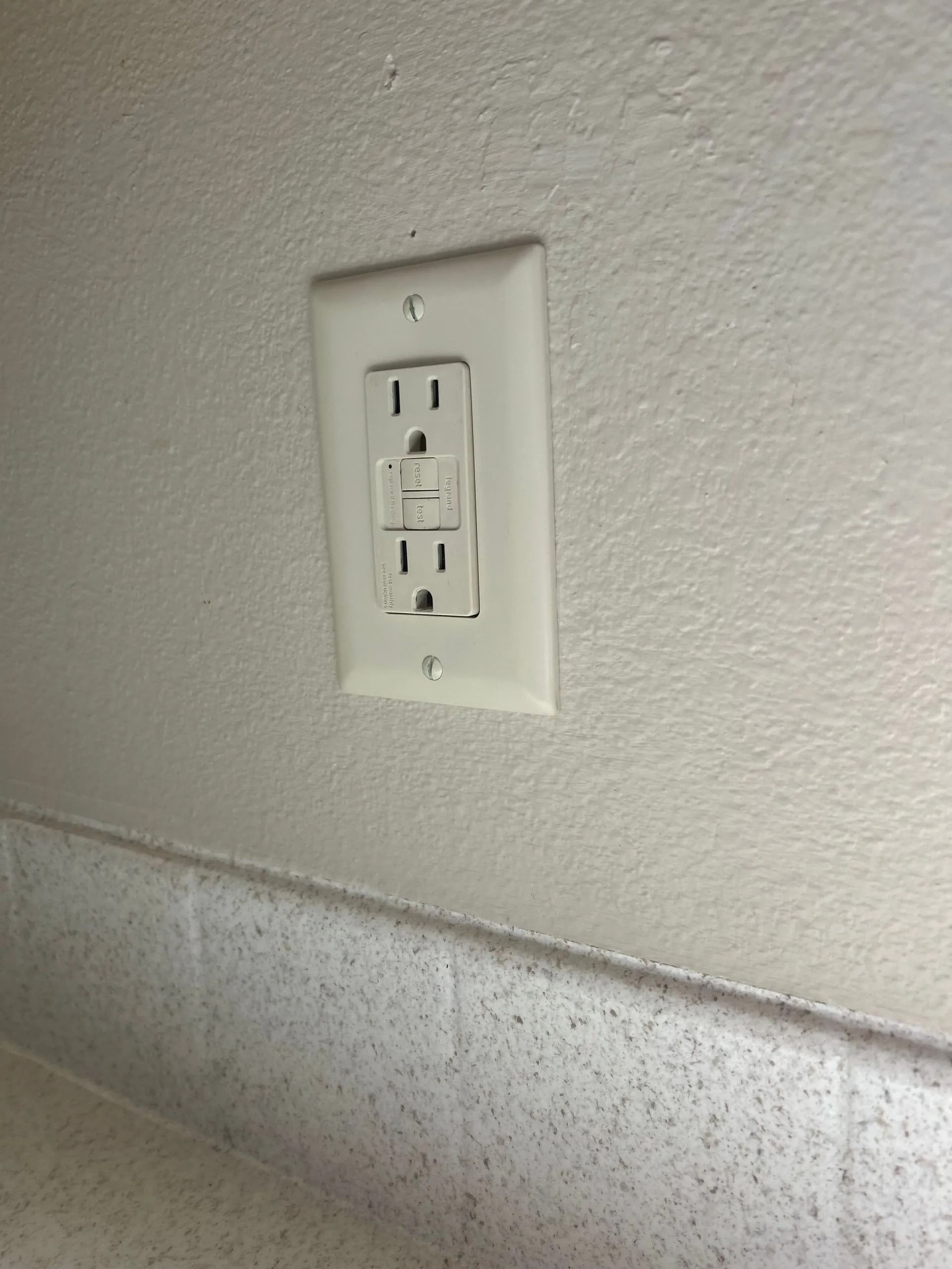 White GFCI outlet on a white wall above a countertop.