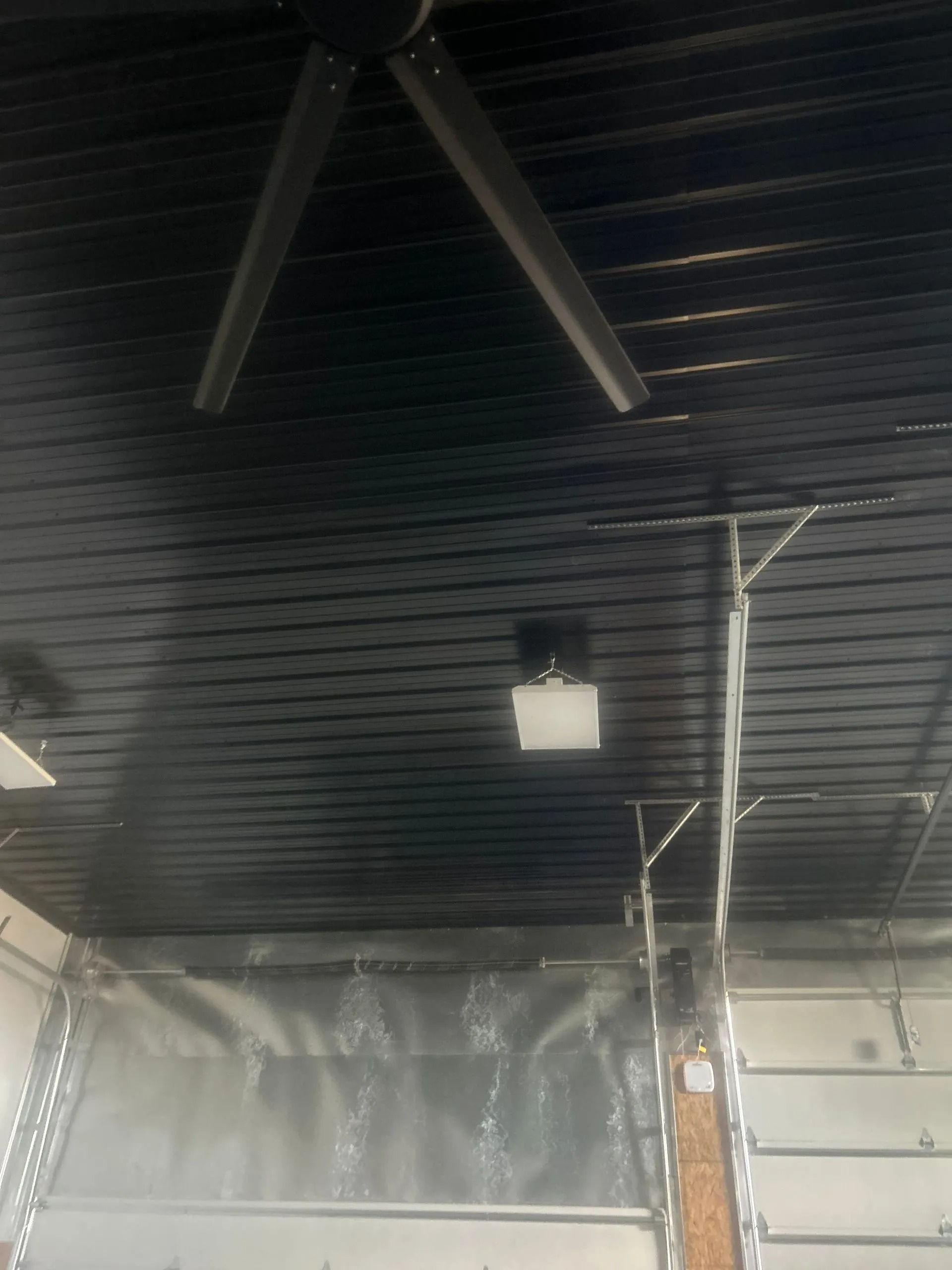 Black ceiling with large fan, light fixture, and garage door partially open.