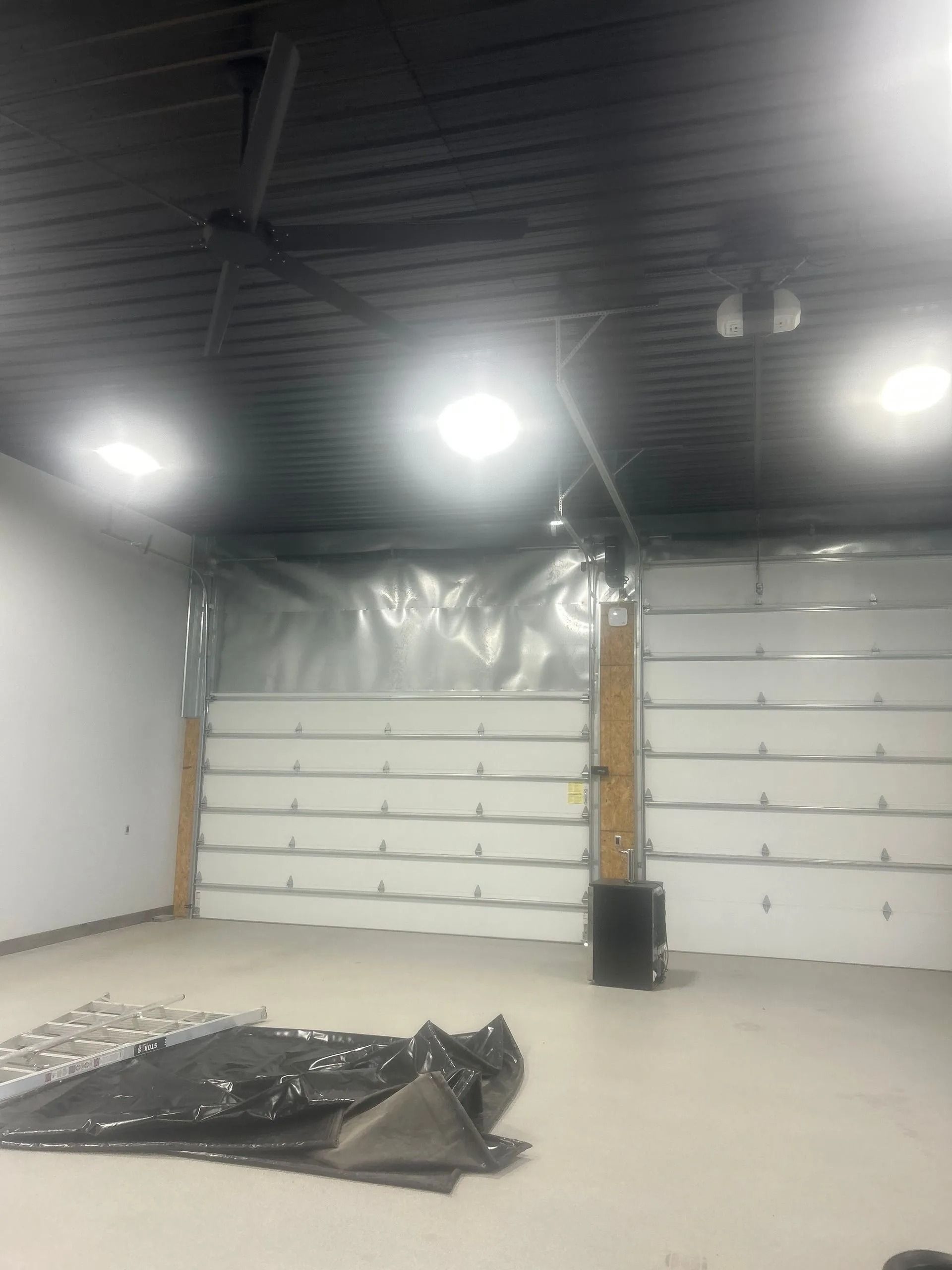 Empty interior of a garage with a closed garage door. Black ceiling and white walls. Lights are on.