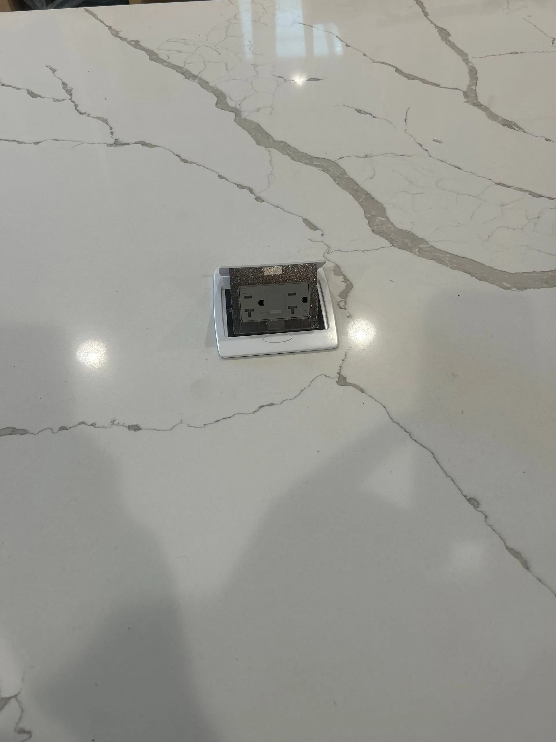 A close-up of a white quartz countertop with a power outlet. Cracks and veins run through the stone.