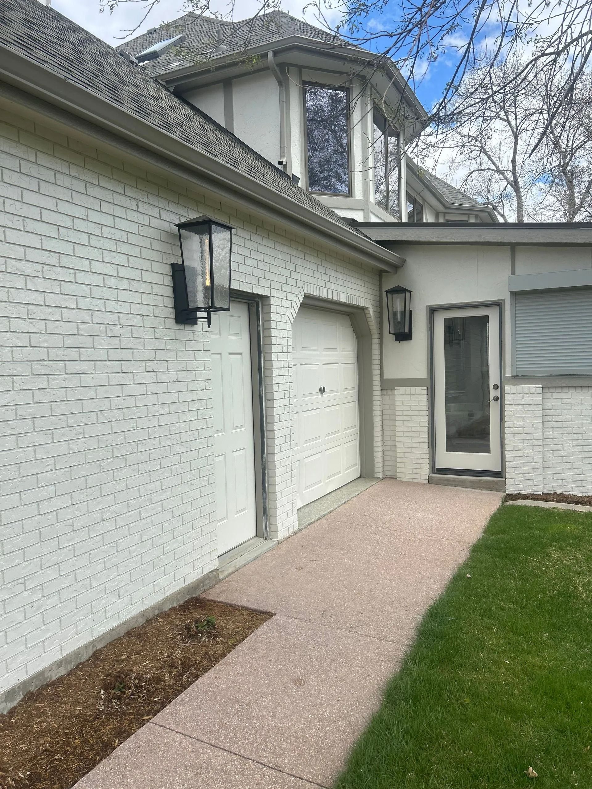 Brick house exterior with white garage doors, a walkway, and black light fixtures.