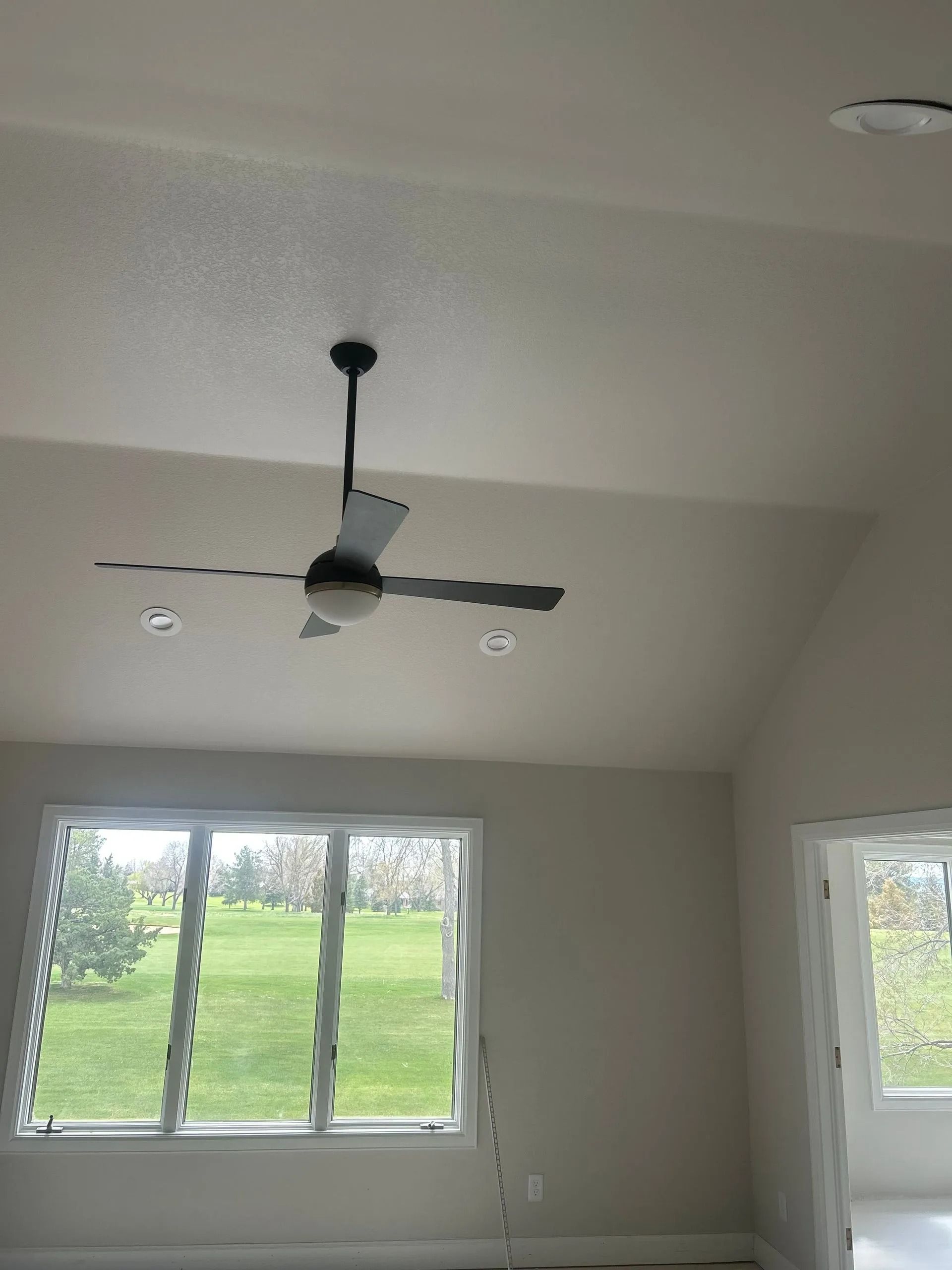 Ceiling fan in a room with a large window overlooking a grassy area.