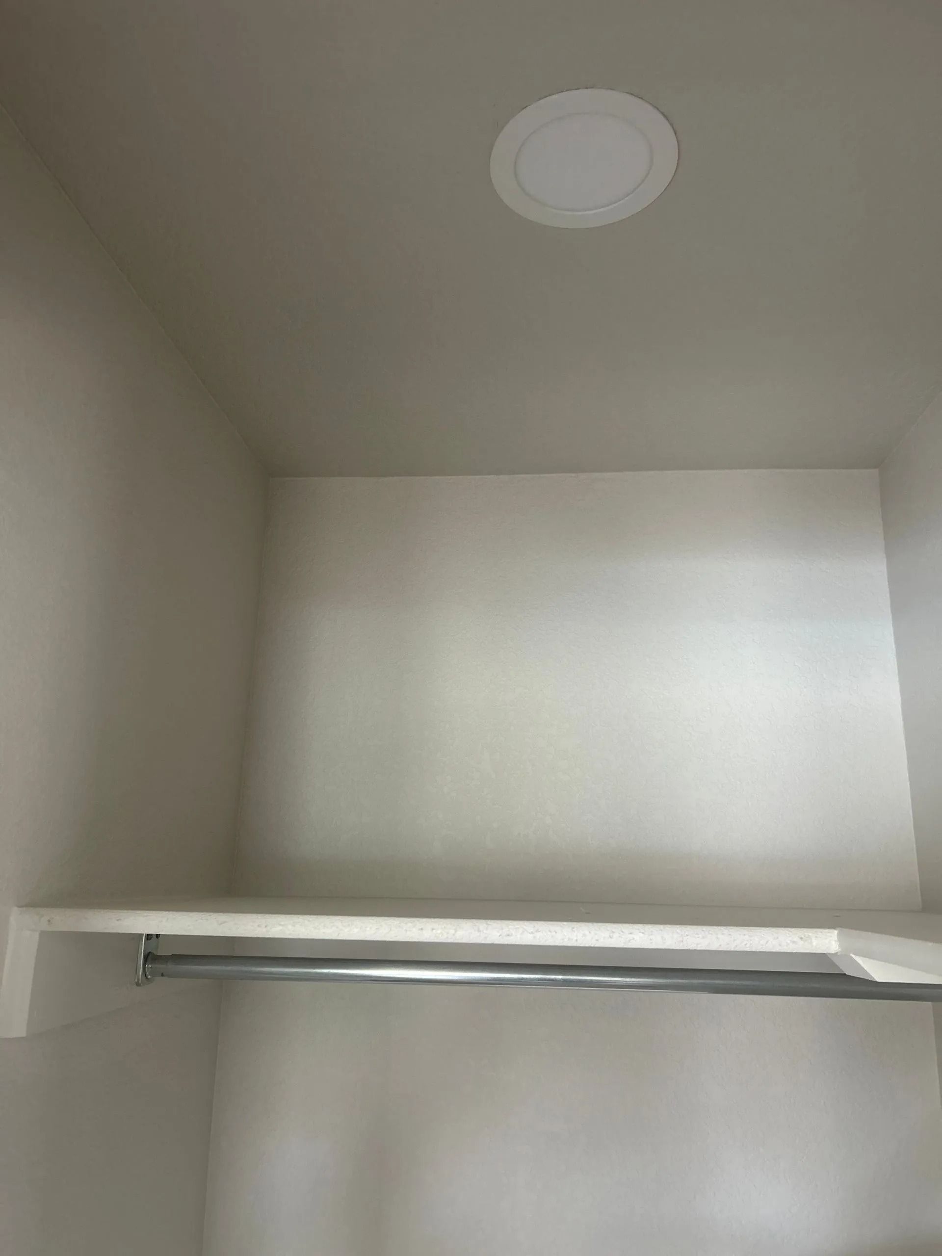 Empty closet interior with a shelf, a metal rod, and a ceiling light.