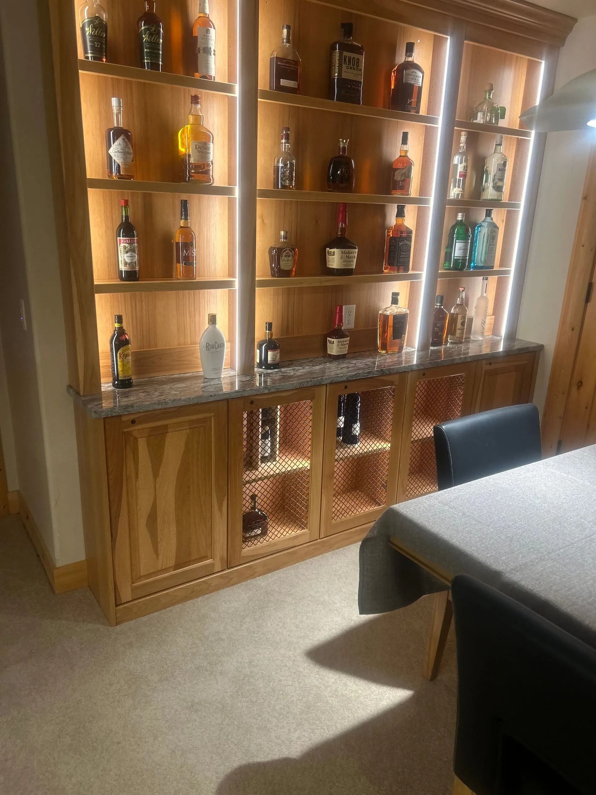 Wooden liquor cabinet with lit shelves displaying various bottles.