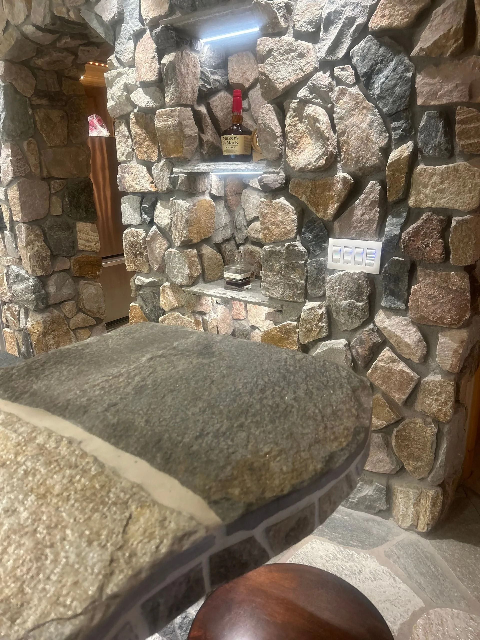 Stone-walled interior with a stone table. A small shelf displays objects, lit from above.