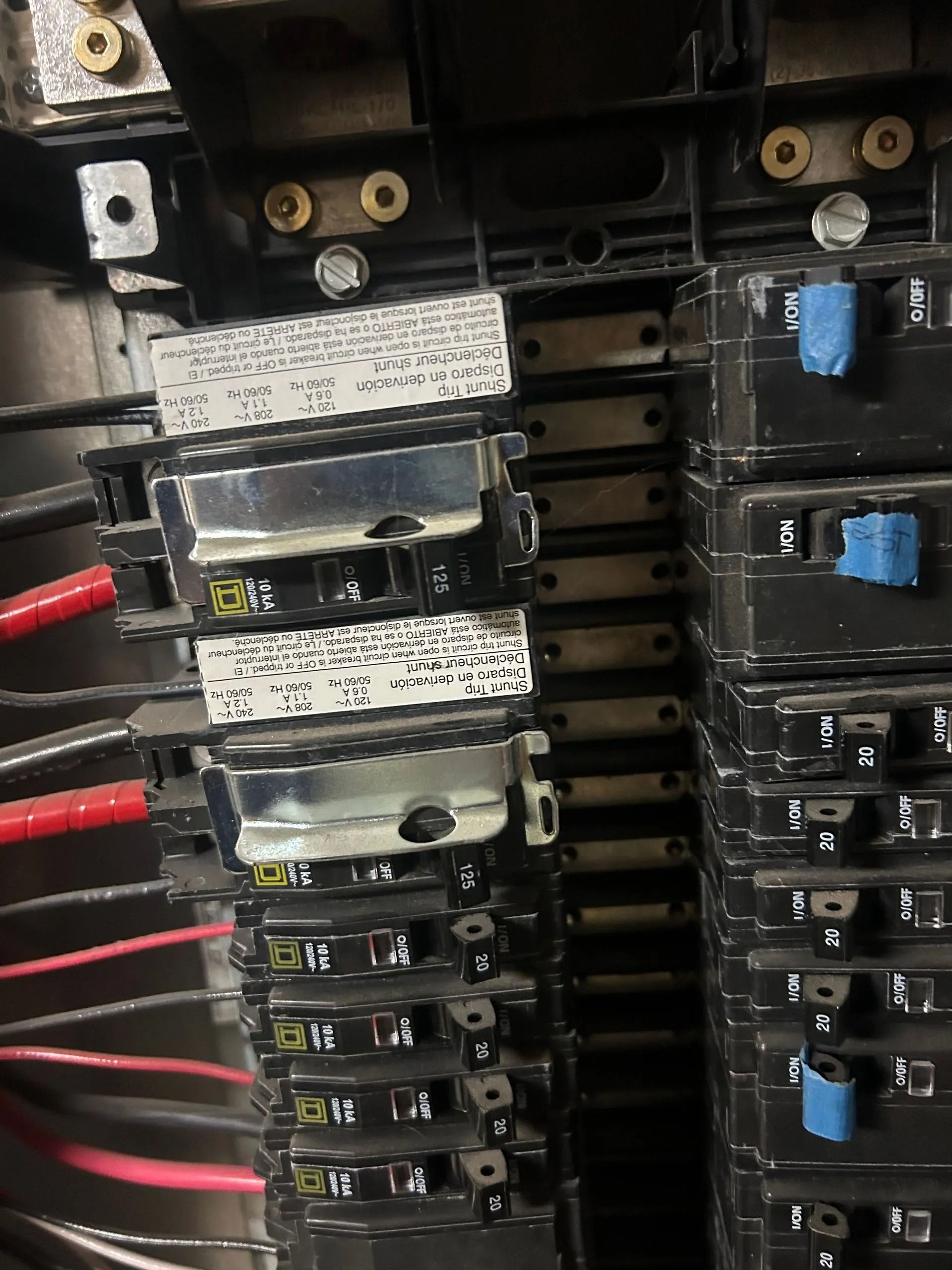 Electrical panel with black circuit breakers, red and black wires visible.
