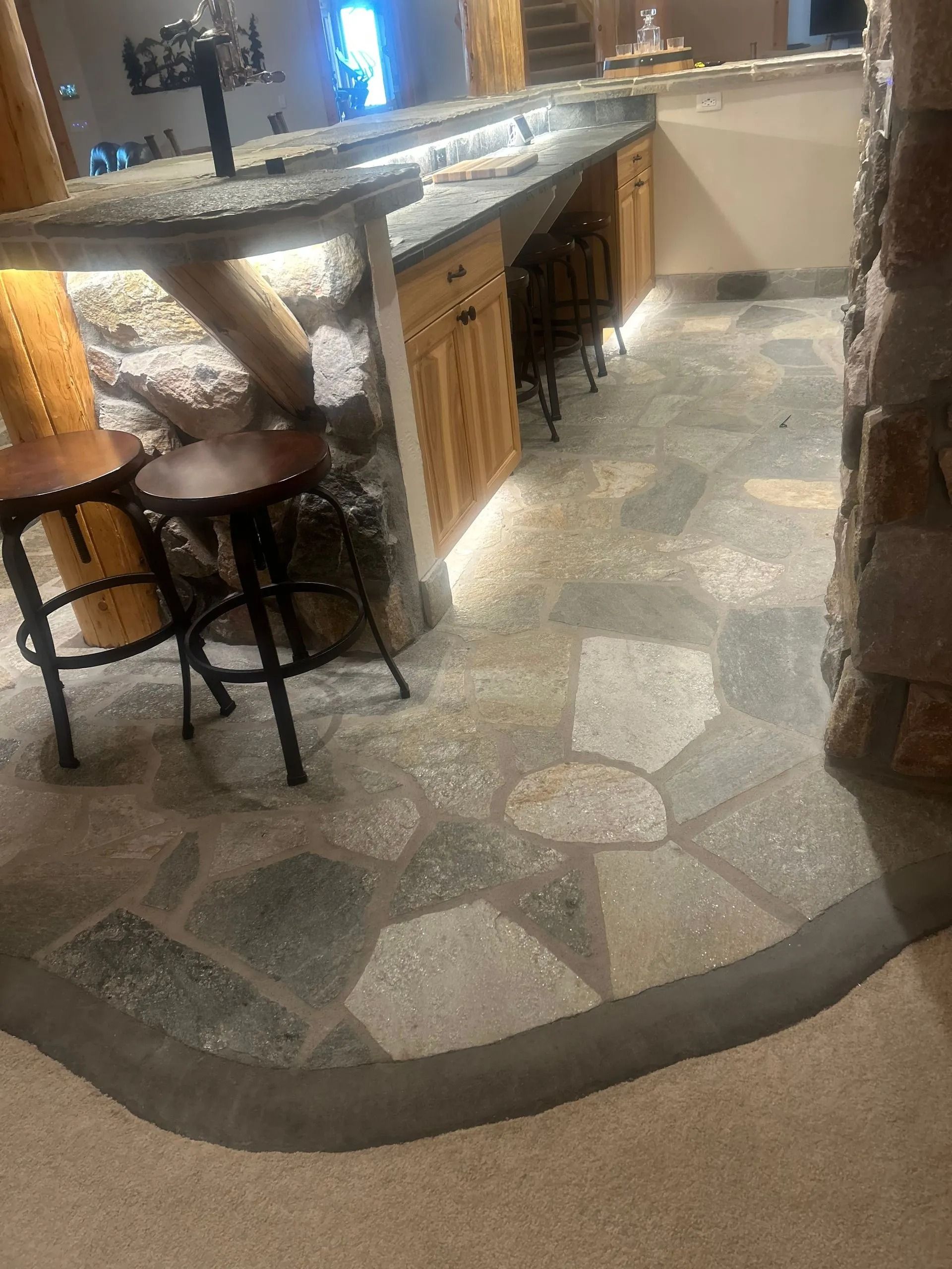 Stone tile floor in front of a bar area with wooden cabinets and stools.