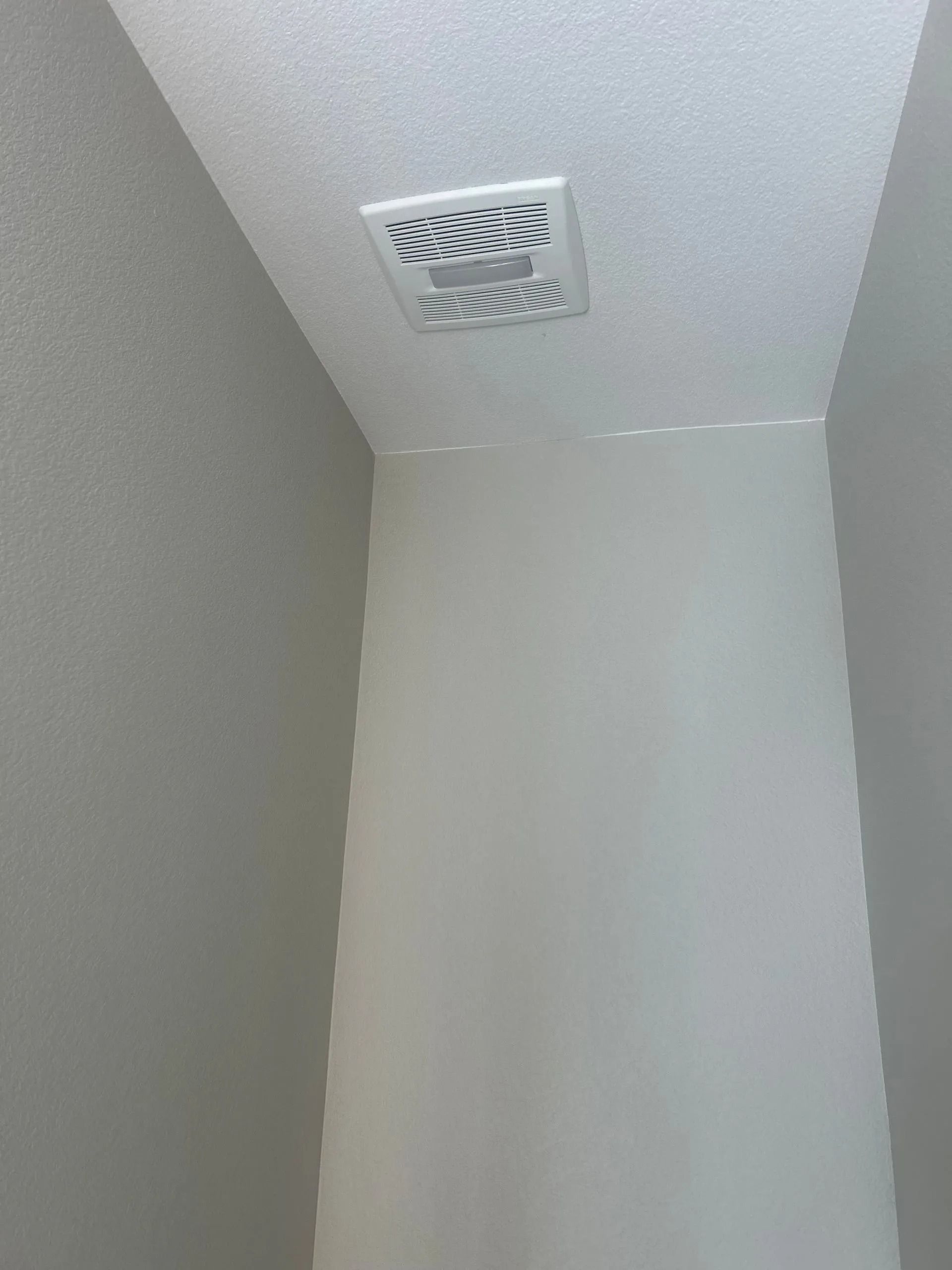 White bathroom ceiling with an exhaust fan. White walls.