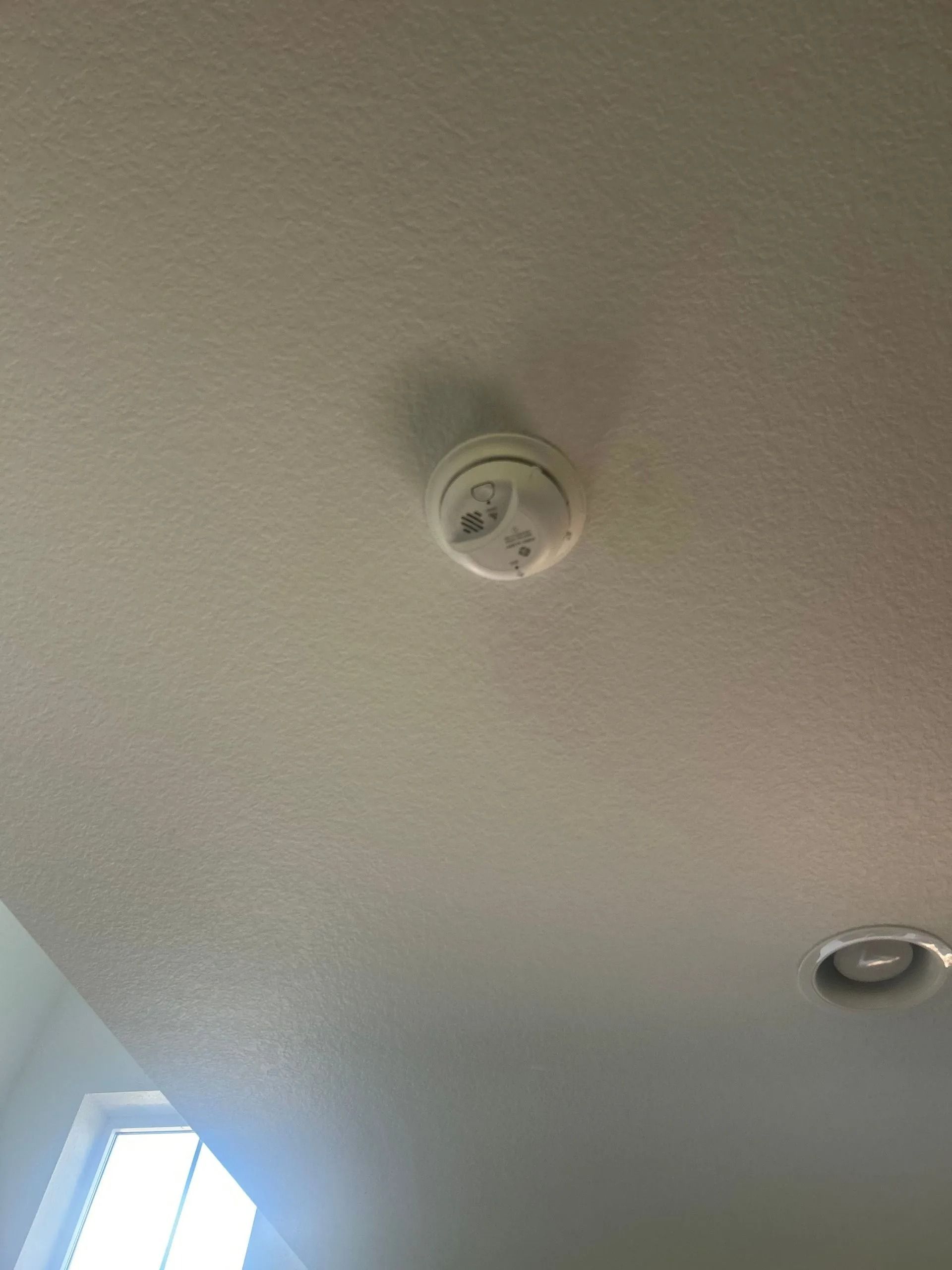 White smoke detector mounted on a white ceiling.