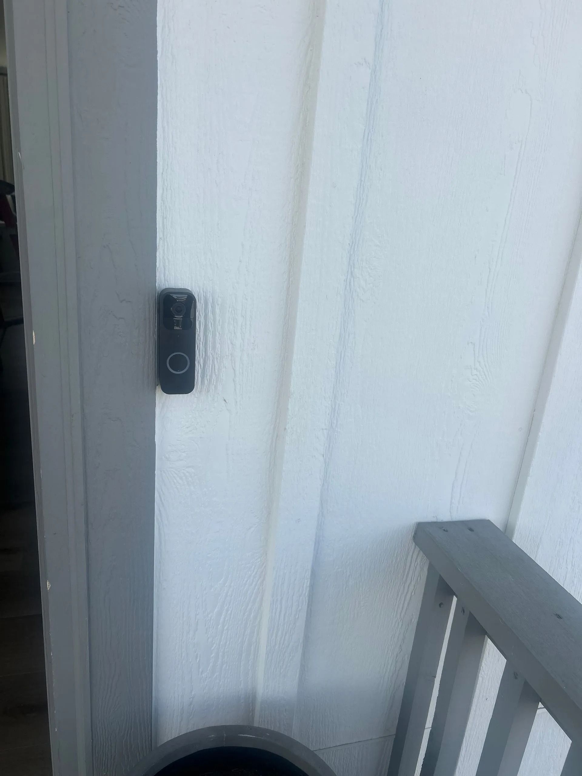 A black doorbell mounted on a white exterior wall next to a porch railing.
