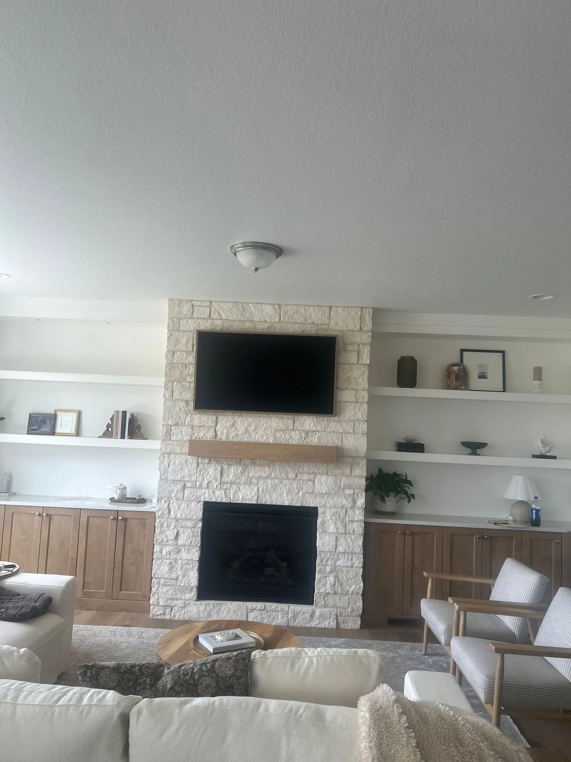 Living room with stone fireplace, TV, built-in shelves, wood cabinets, and seating.