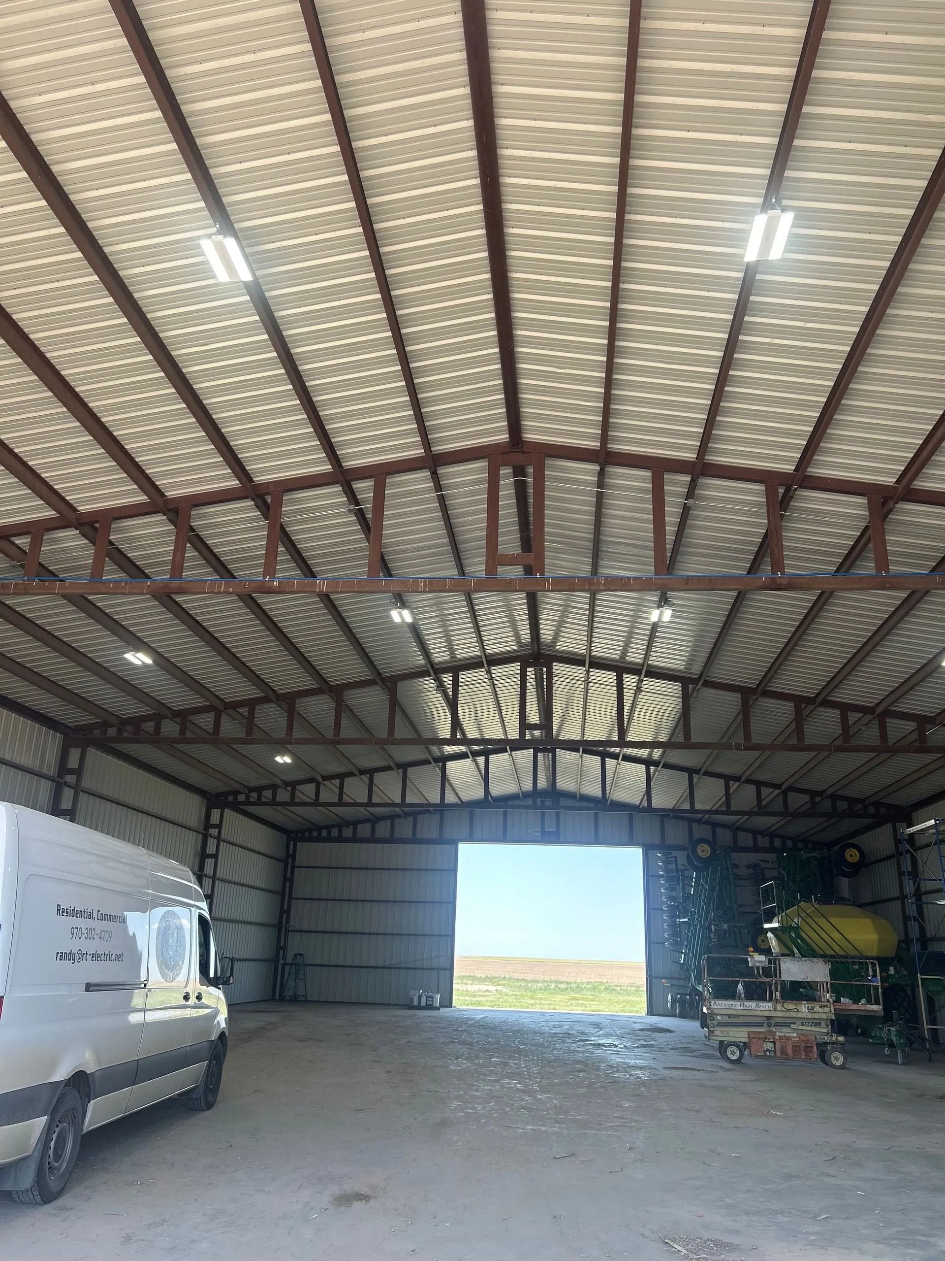 Inside a metal industrial building with a large open doorway, a vehicle is parked.
