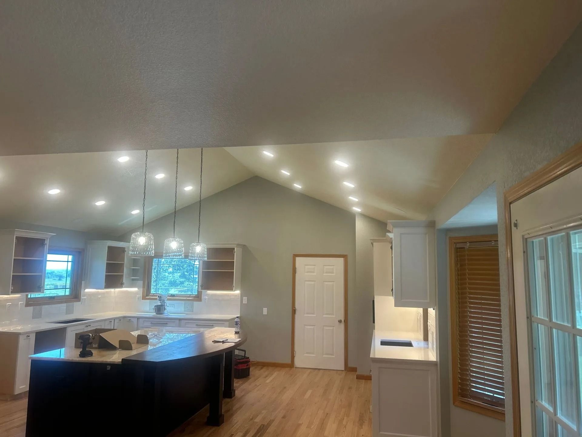 Kitchen with vaulted ceiling, recessed lights, cabinets, island, and door.