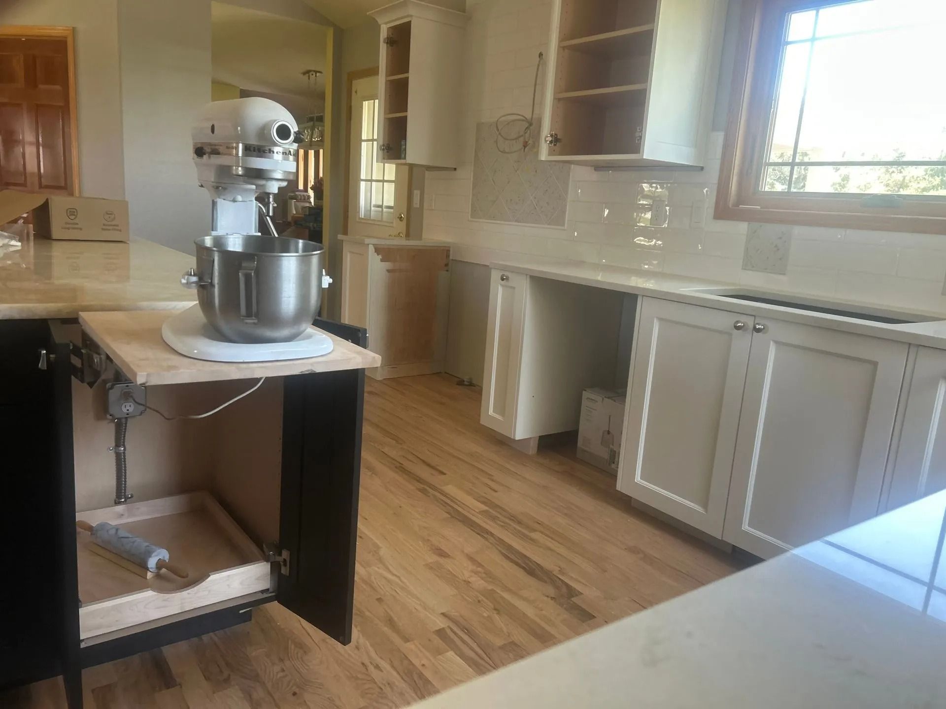 Kitchen with a built-in appliance lift holding a stand mixer. Cabinets are light, countertops are white.