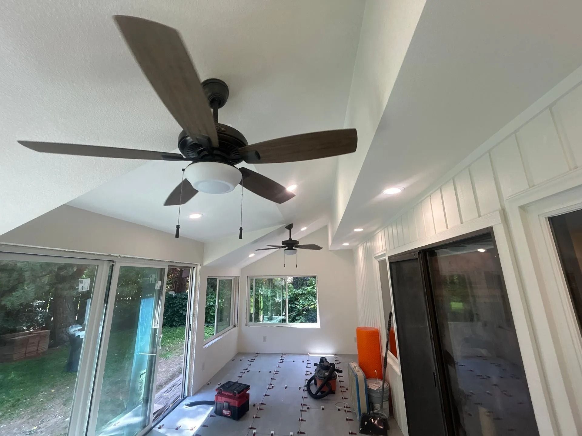 Sunroom interior with two ceiling fans, recessed lighting, and windows overlooking a yard.