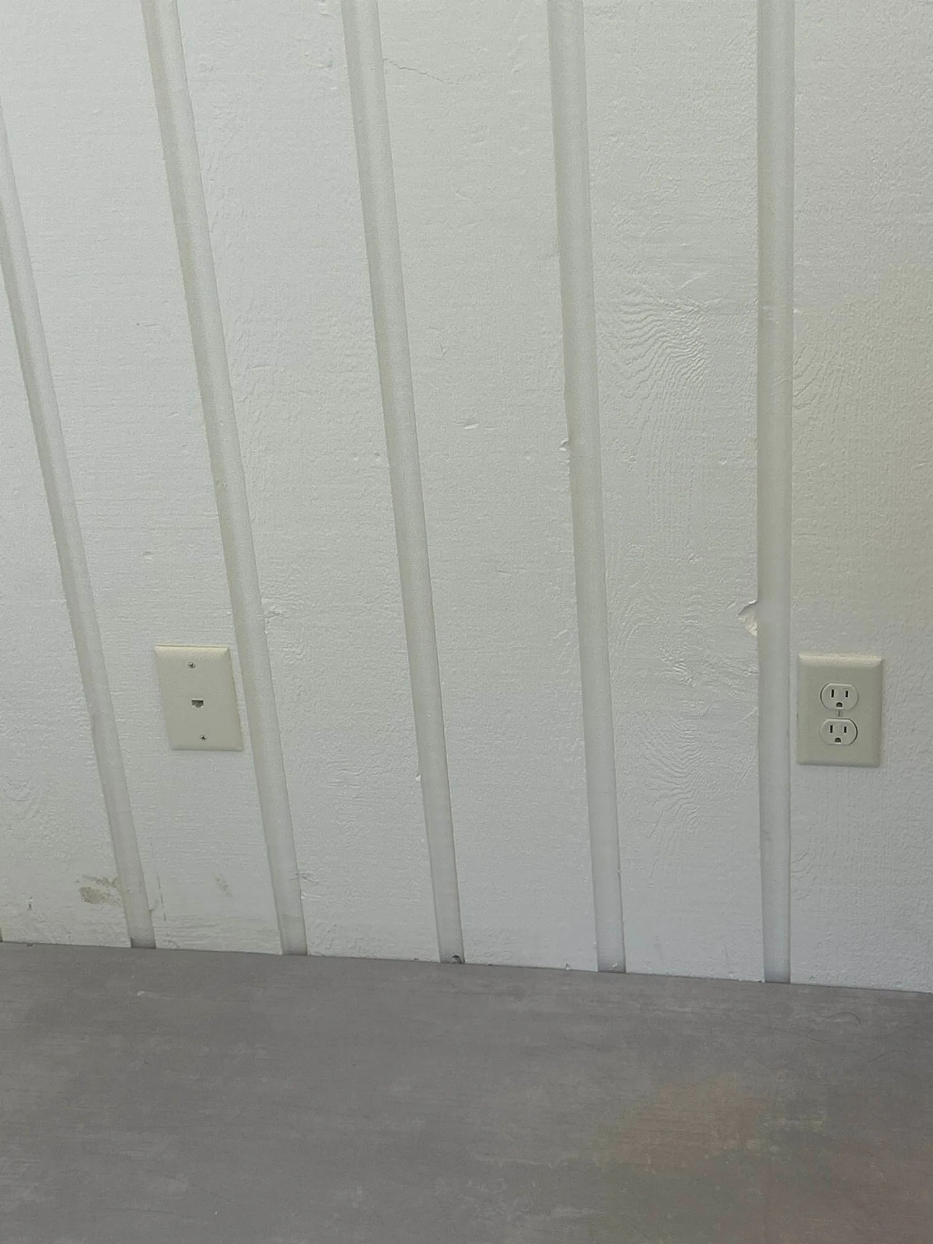 White-painted wood paneling with two electrical outlets along a gray floor.