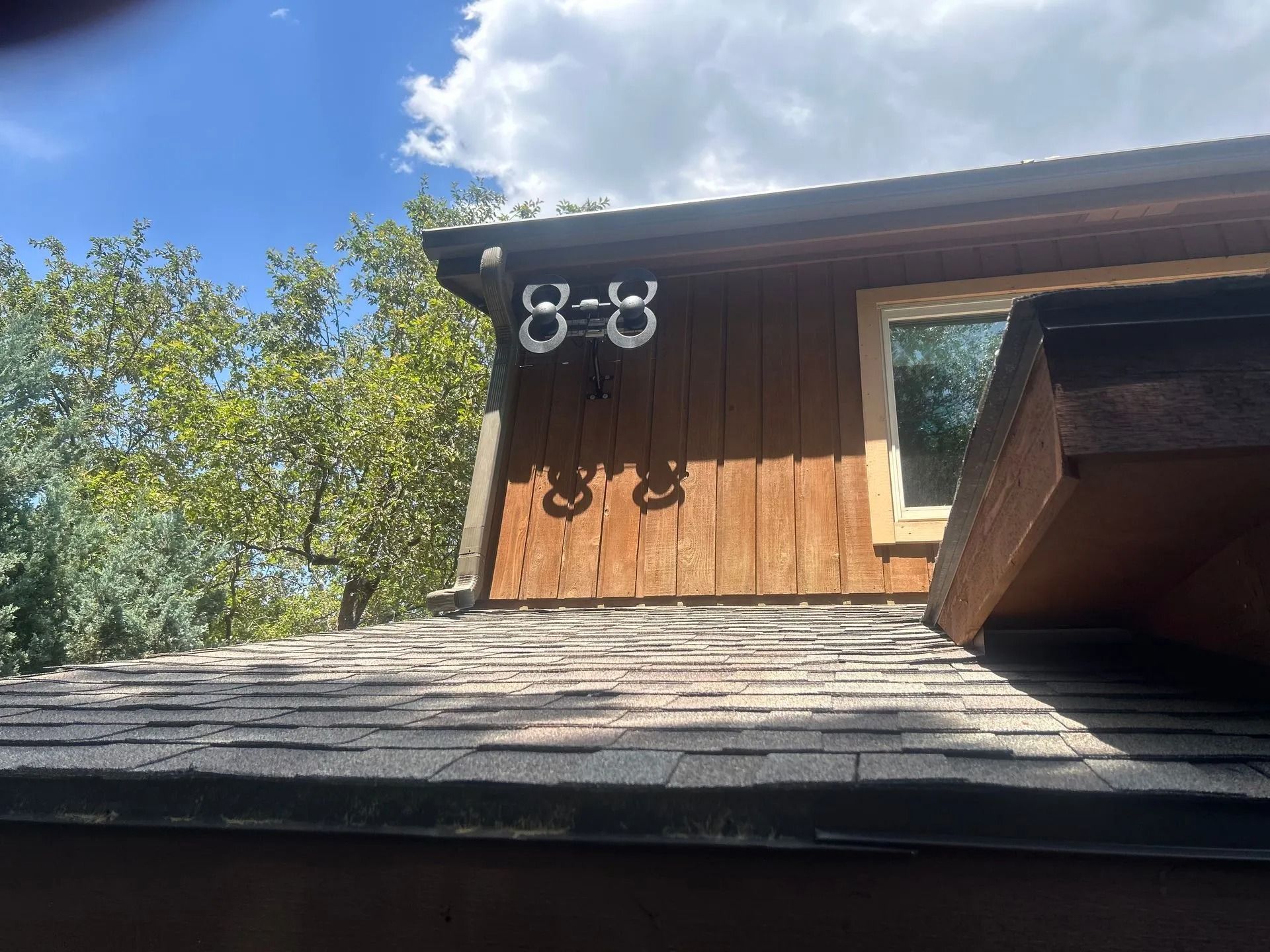 Security cameras mounted on a wood-paneled building, above a shingled roof, against a blue sky.
