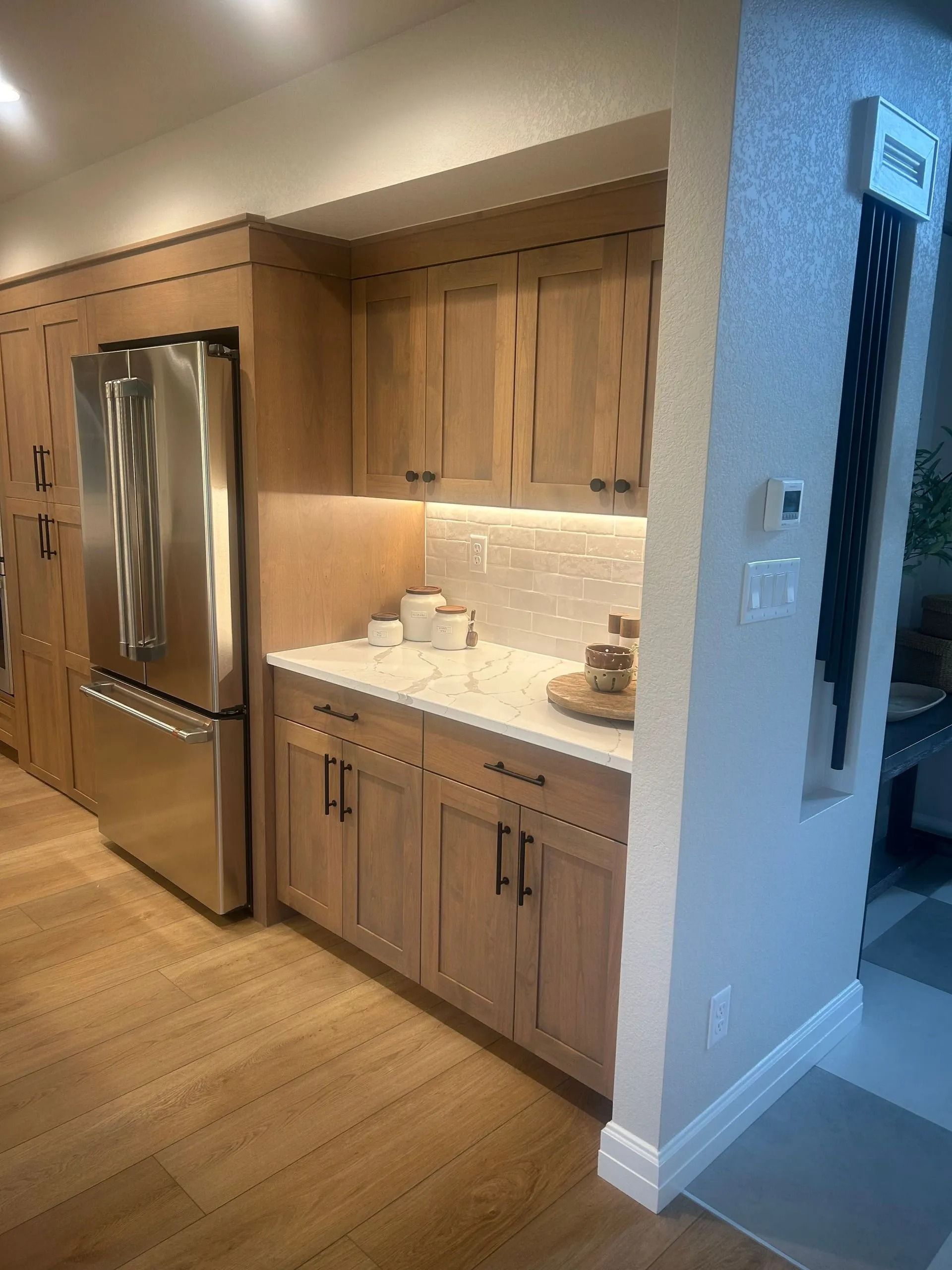 Kitchenette with light wood cabinets, stainless steel refrigerator, and white countertops.
