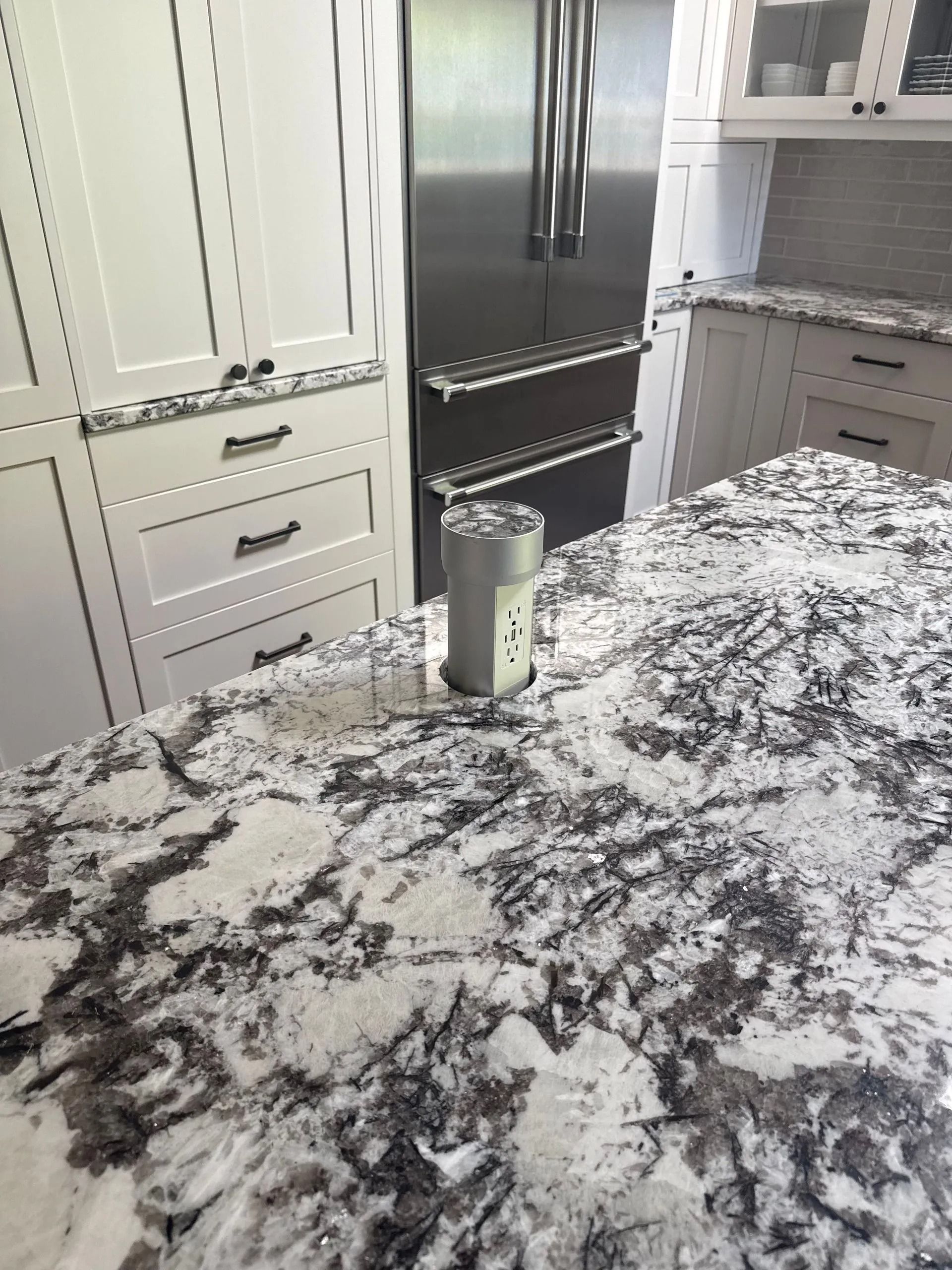Kitchen with a granite countertop and stainless steel refrigerator. A spice container sits on the counter.