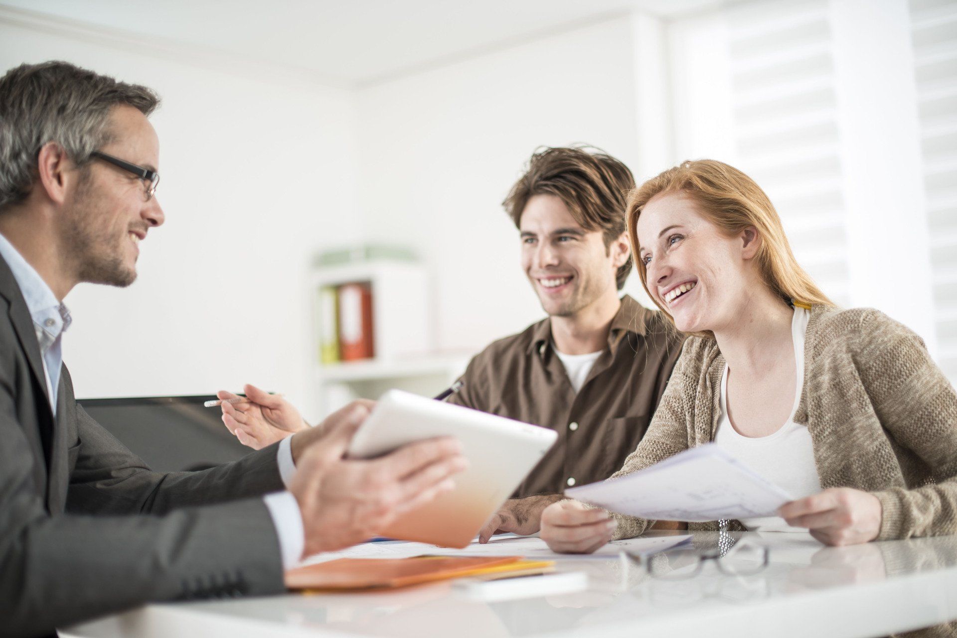 A financial advisor shows paperwork to a smiling couple at a desk.