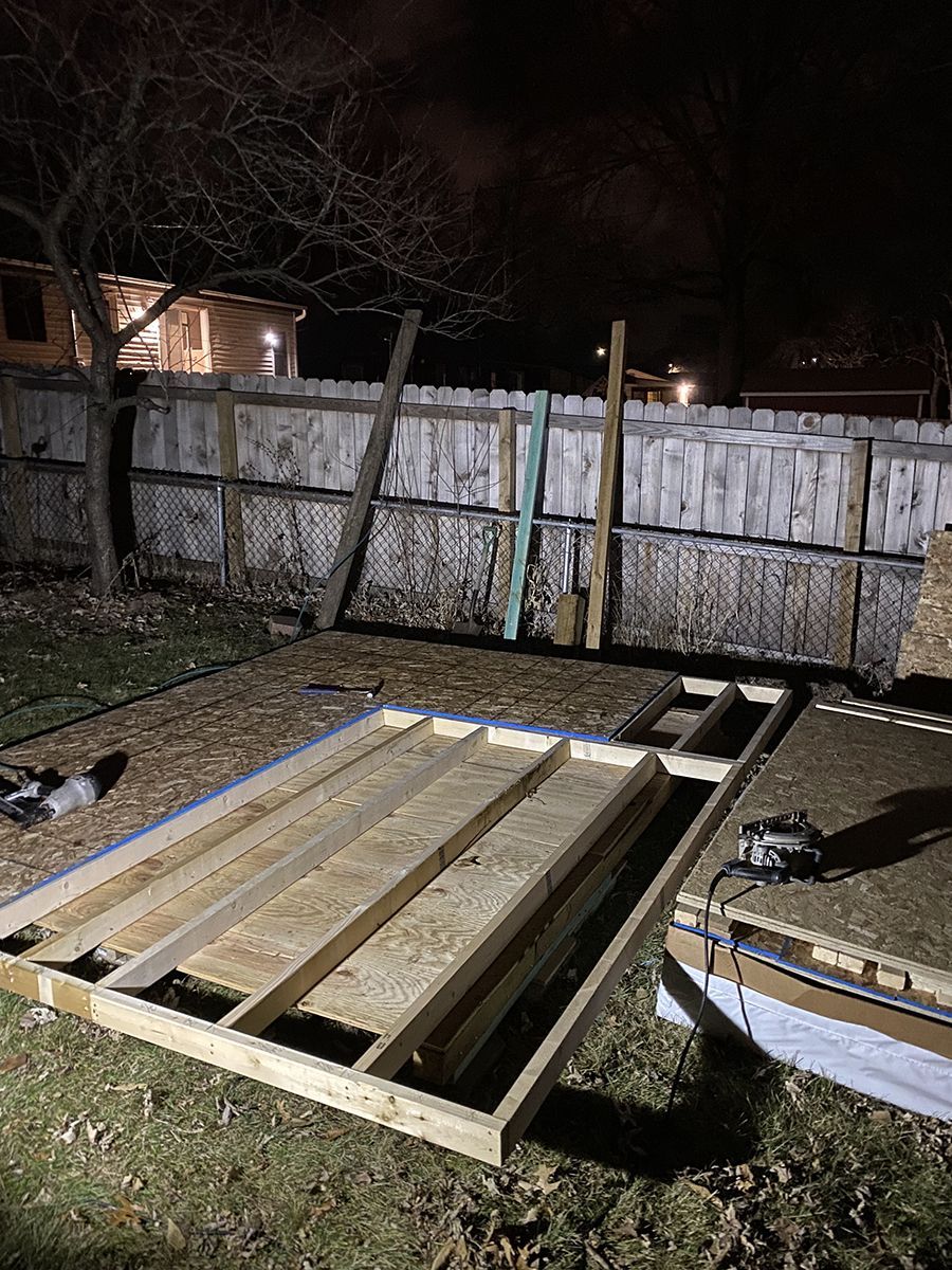 A wooden structure is being built in a backyard at night.