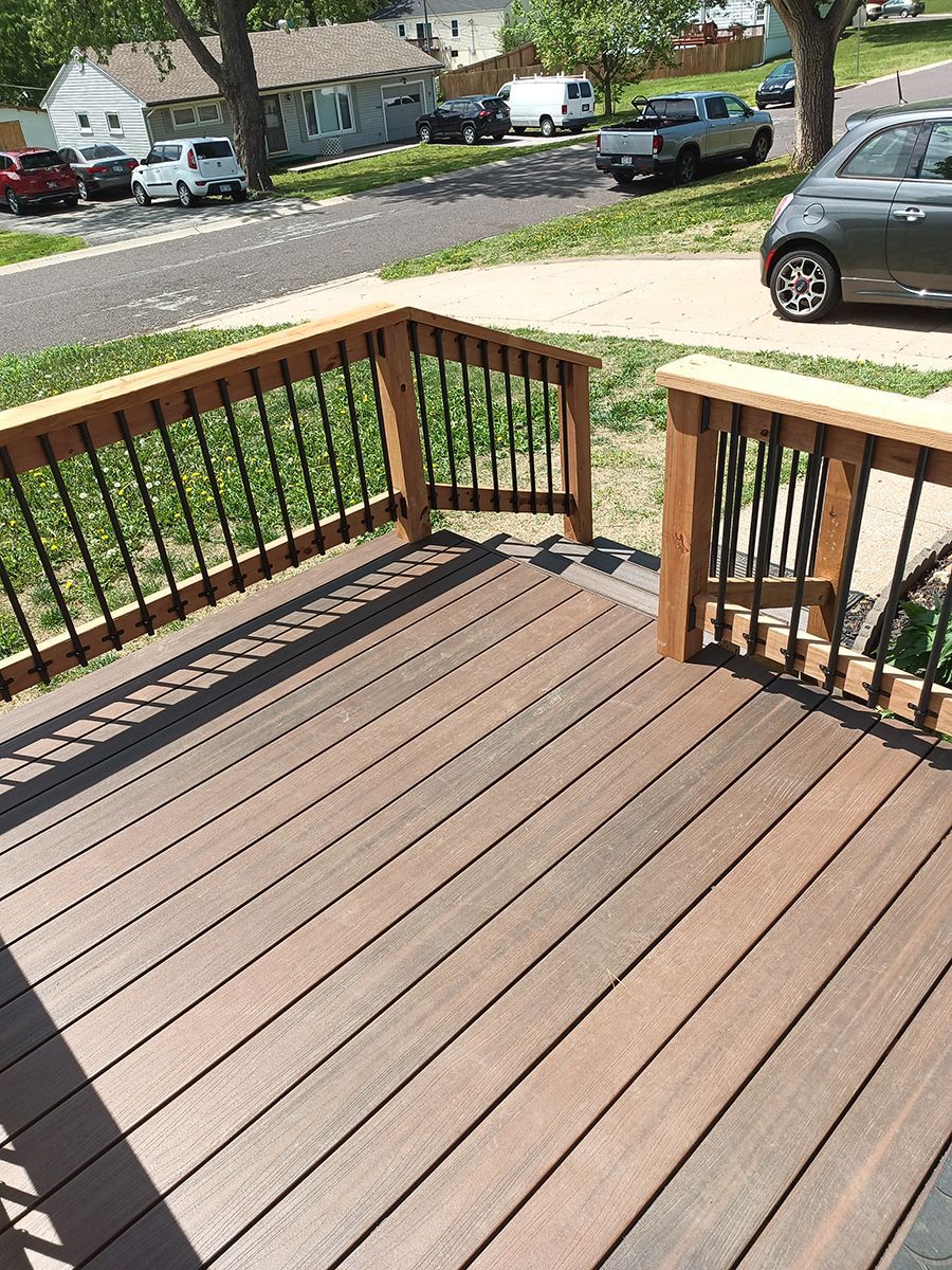 A wooden deck with a metal railing and a car parked on the side of the road.