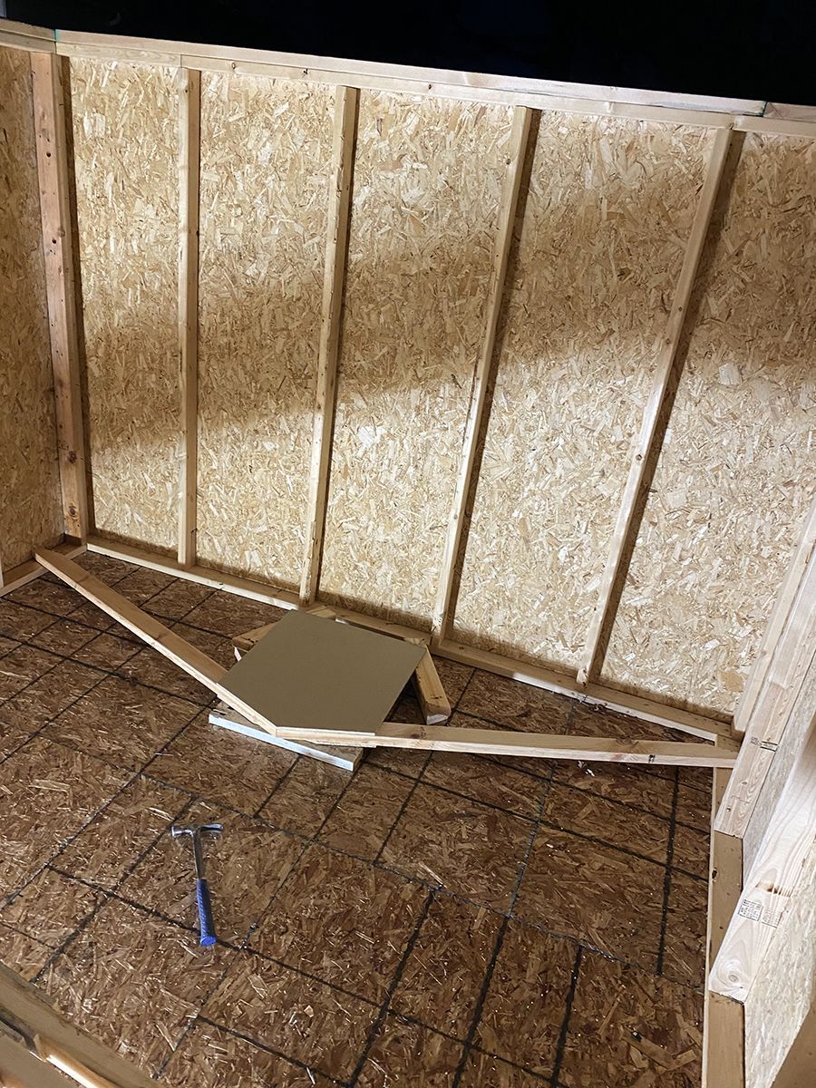 A hammer is laying on the floor next to a wooden wall.