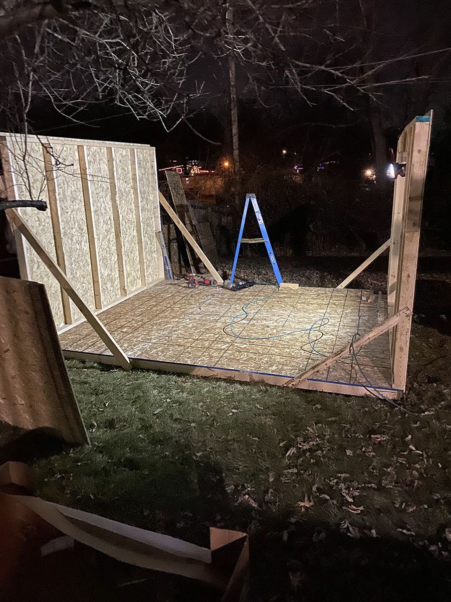 A wooden shed is being built at night in a backyard.