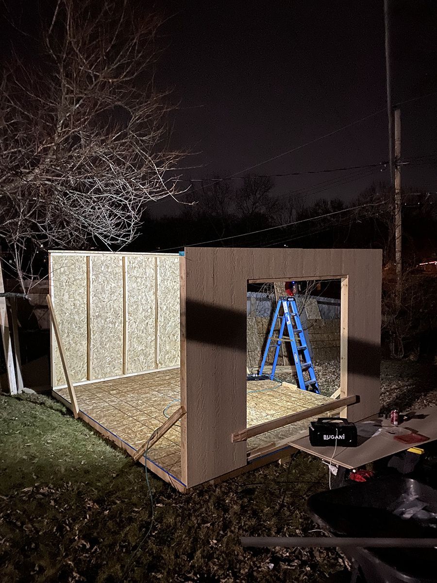A wooden shed is being built at night with a blue ladder.
