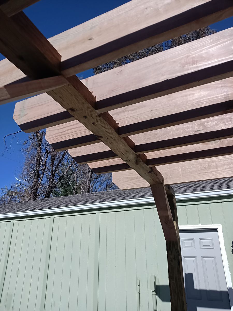 A wooden pergola is being built on the side of a house.