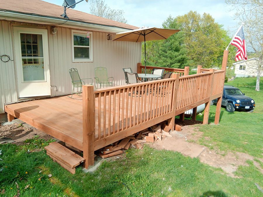 A wooden deck with a table and chairs on it is in front of a house.