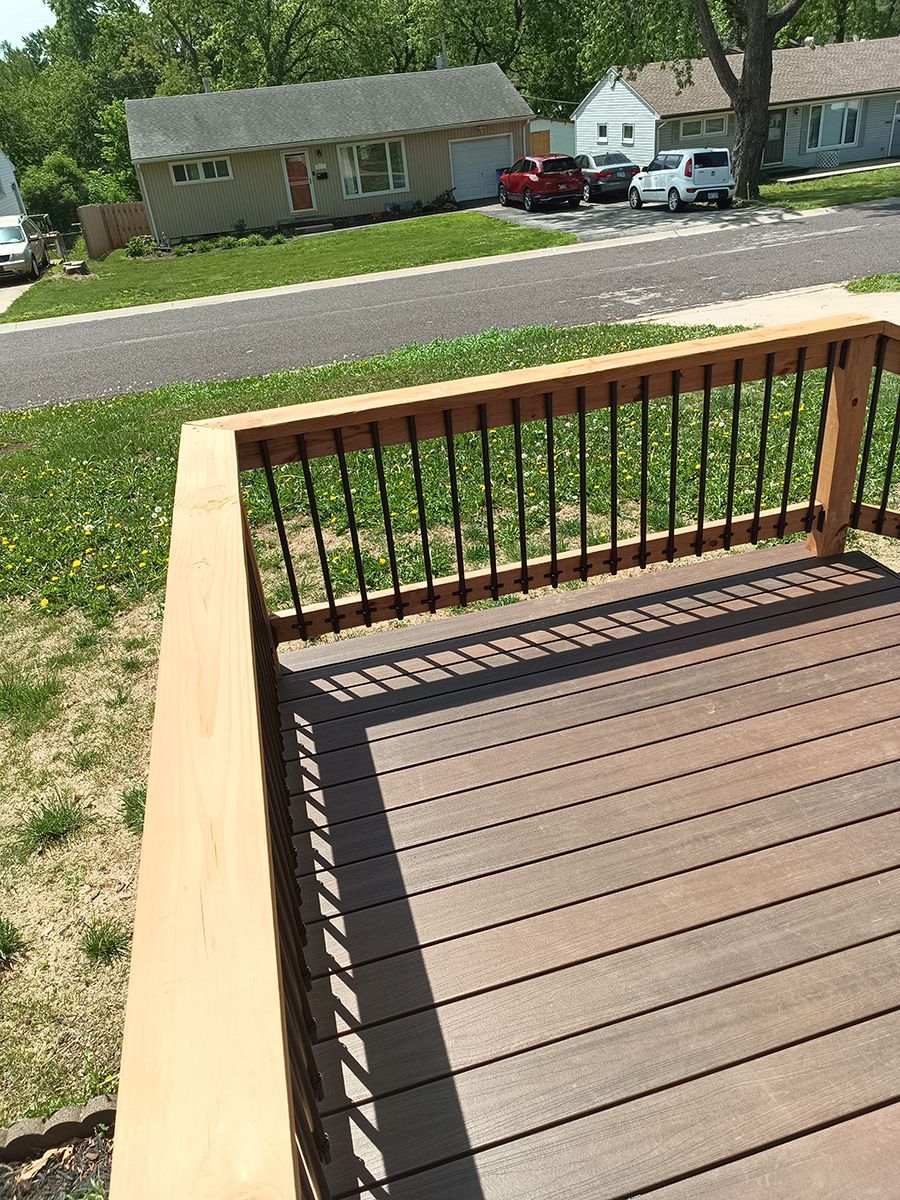 A wooden deck with a metal railing and a house in the background.