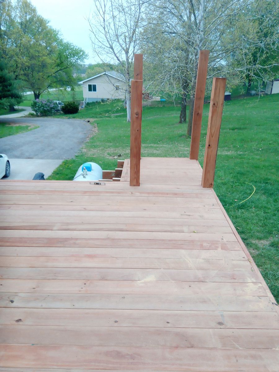 A wooden deck with a car parked in the driveway and a house in the background.