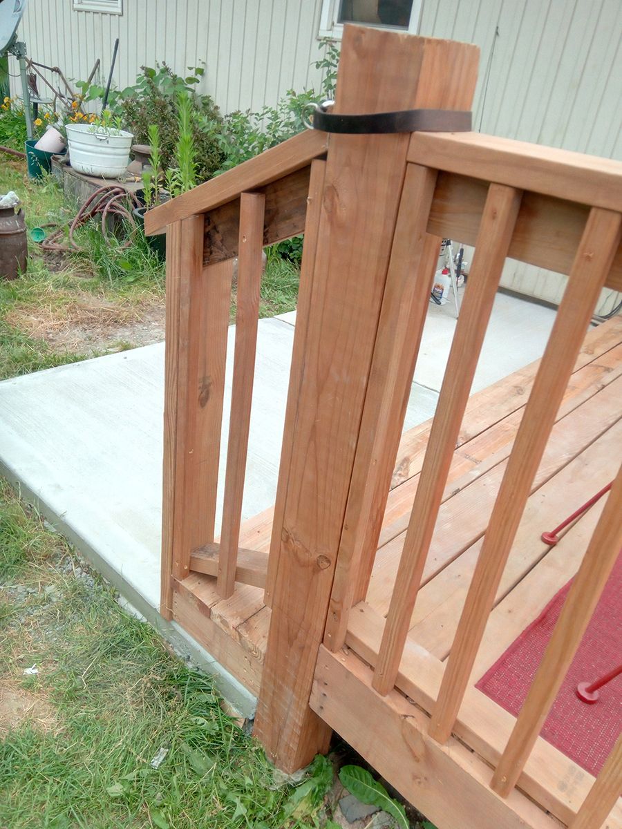A wooden railing on a deck with a concrete walkway leading to it.
