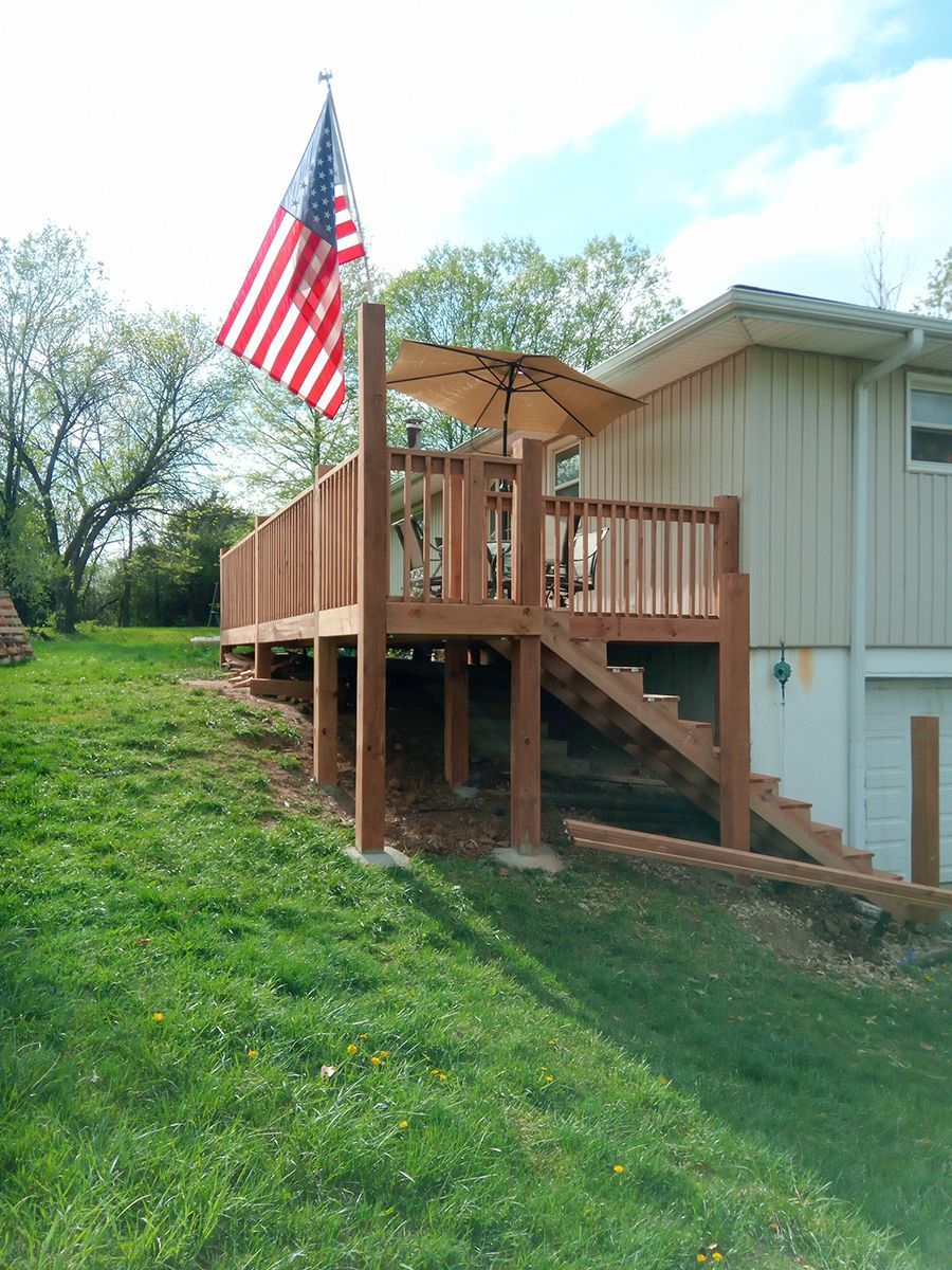 A wooden deck with an American flag and umbrella in front of a house.