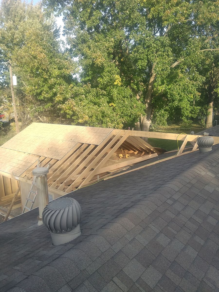 A roof with a wind turbine on top of it and trees in the background.