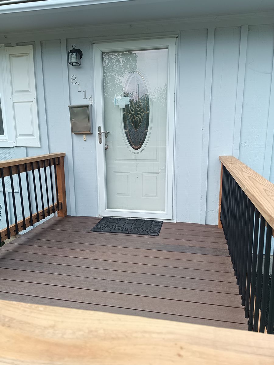 The front door of a house with a wooden deck and stairs leading to it.