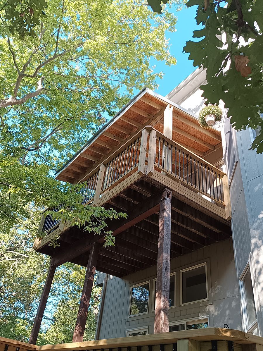 A house with a wooden deck on top of it surrounded by trees.