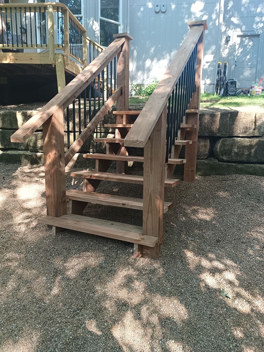 A wooden deck with stairs leading up to it and a house in the background.