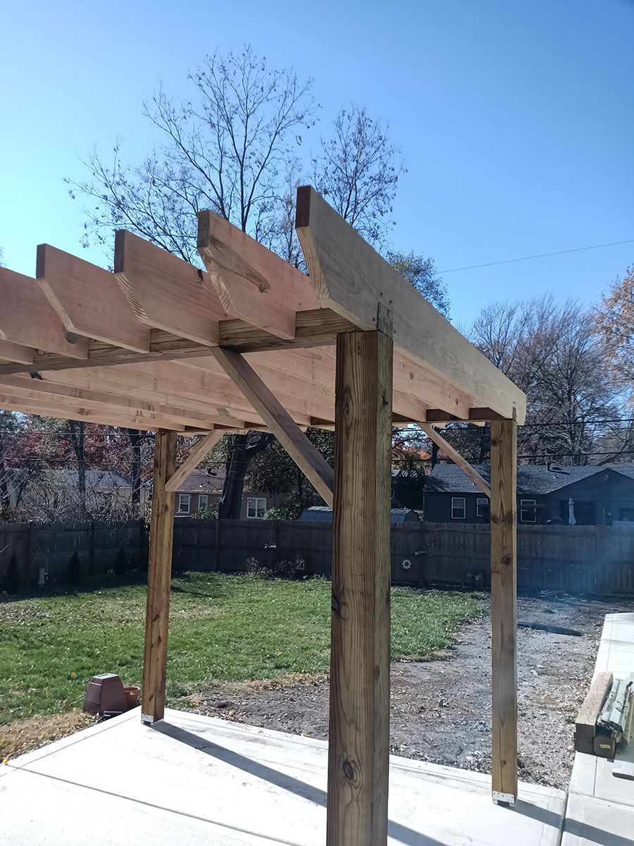 A wooden pergola is sitting on top of a concrete patio in a backyard.