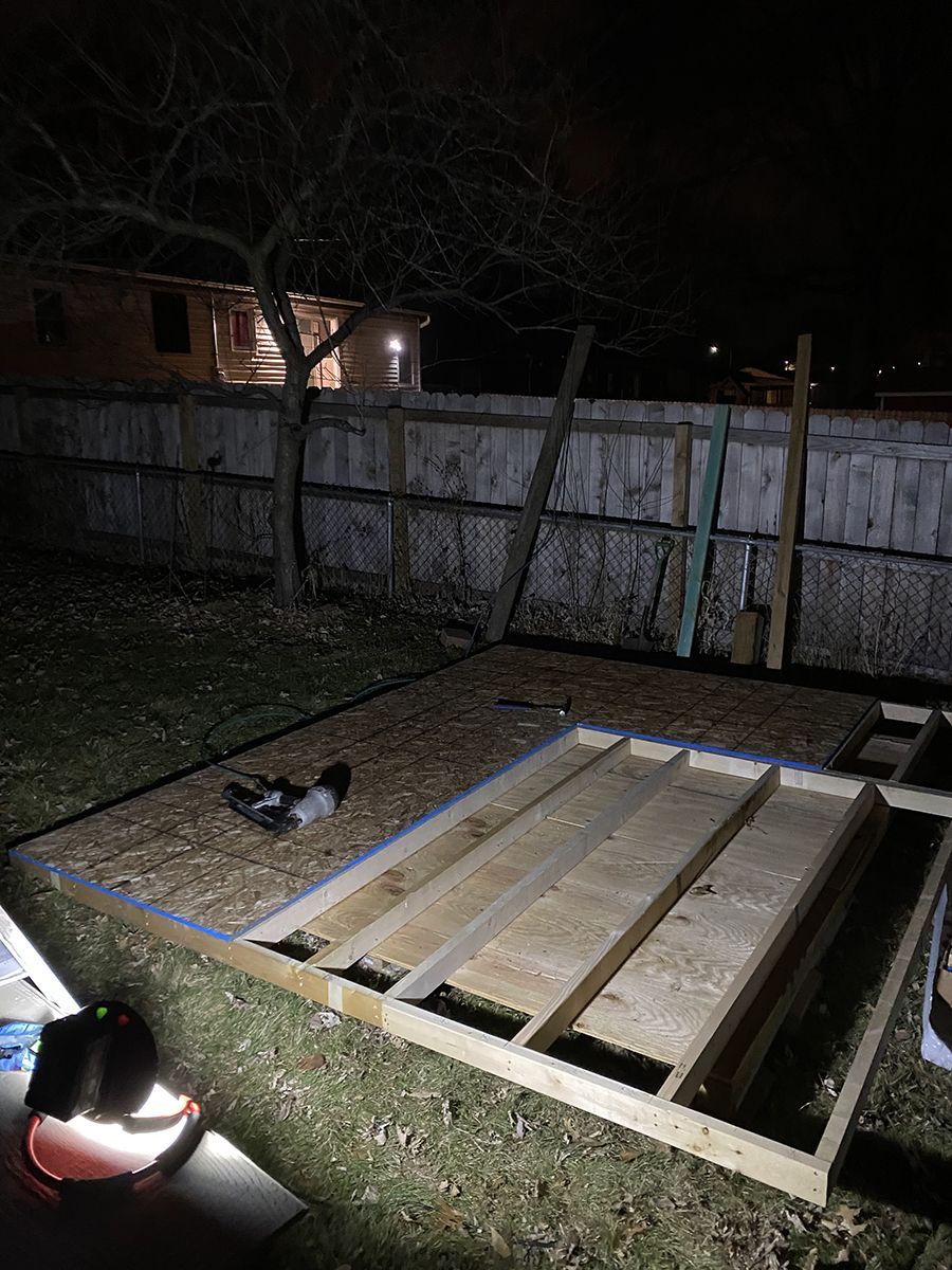 A wooden structure is being built in a backyard at night.